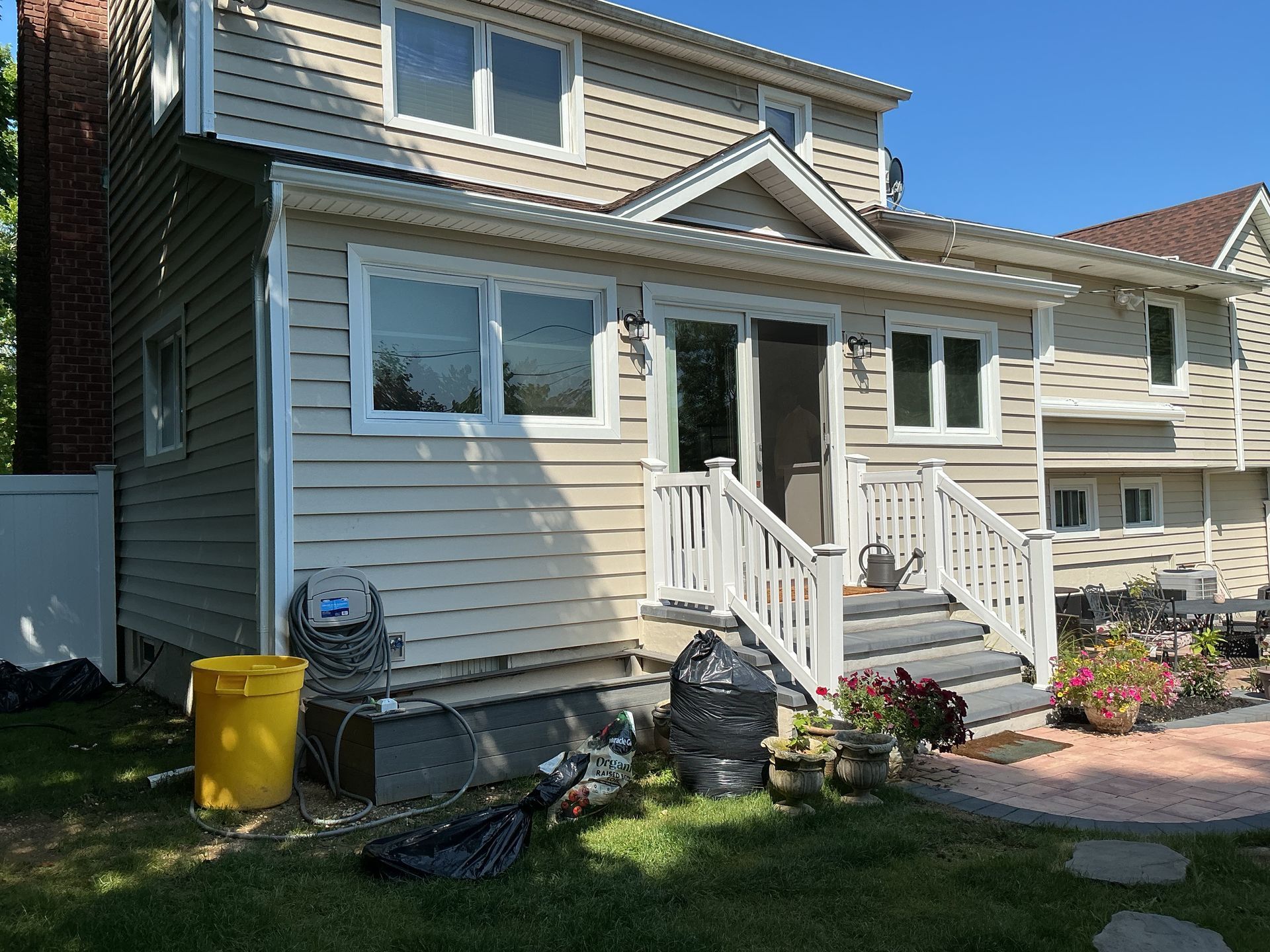 Suburban house exterior with white siding, front steps, windows, and a small garden by the walkway