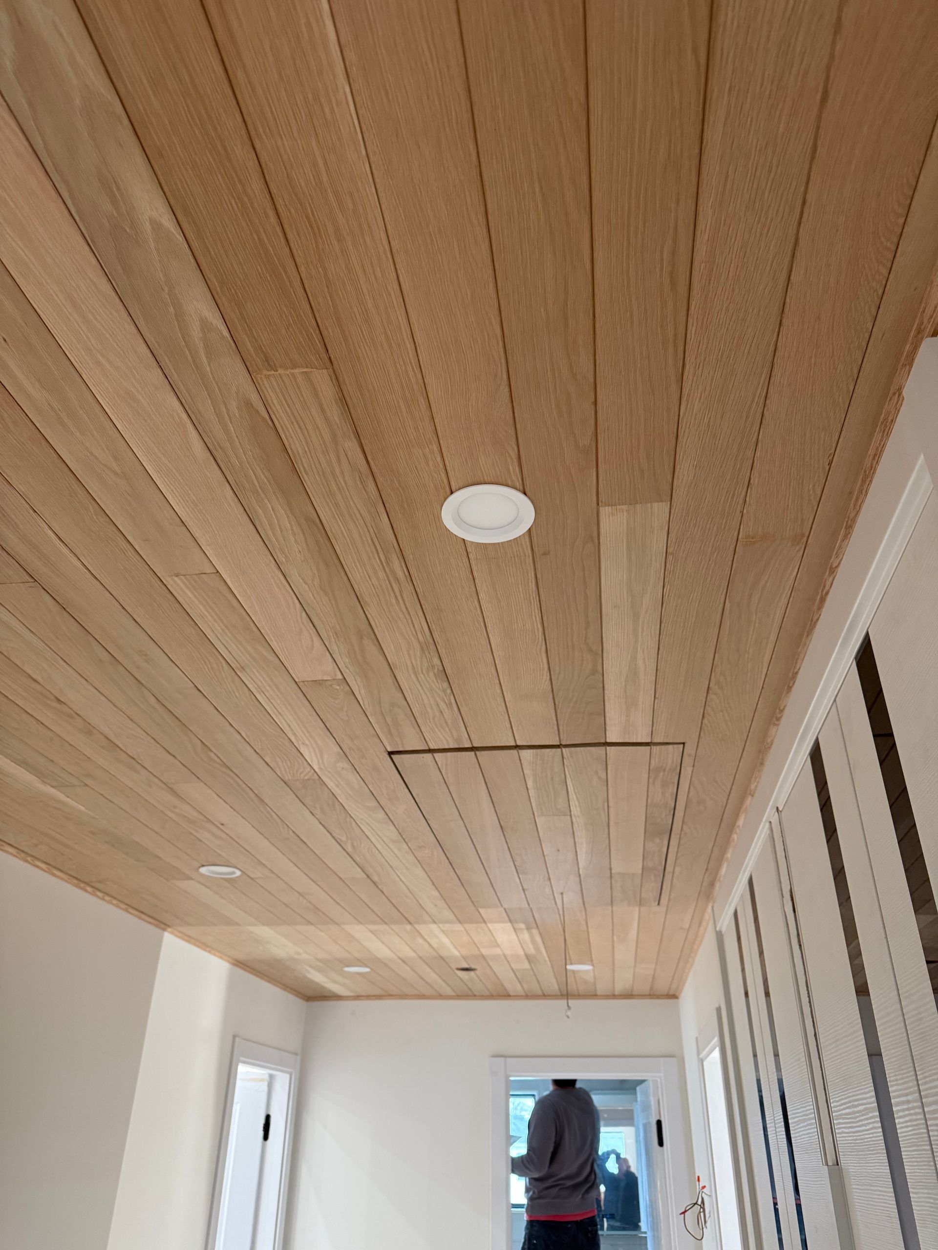 Hallway with wood-paneled ceiling and white walls, one person standing near the far end.
