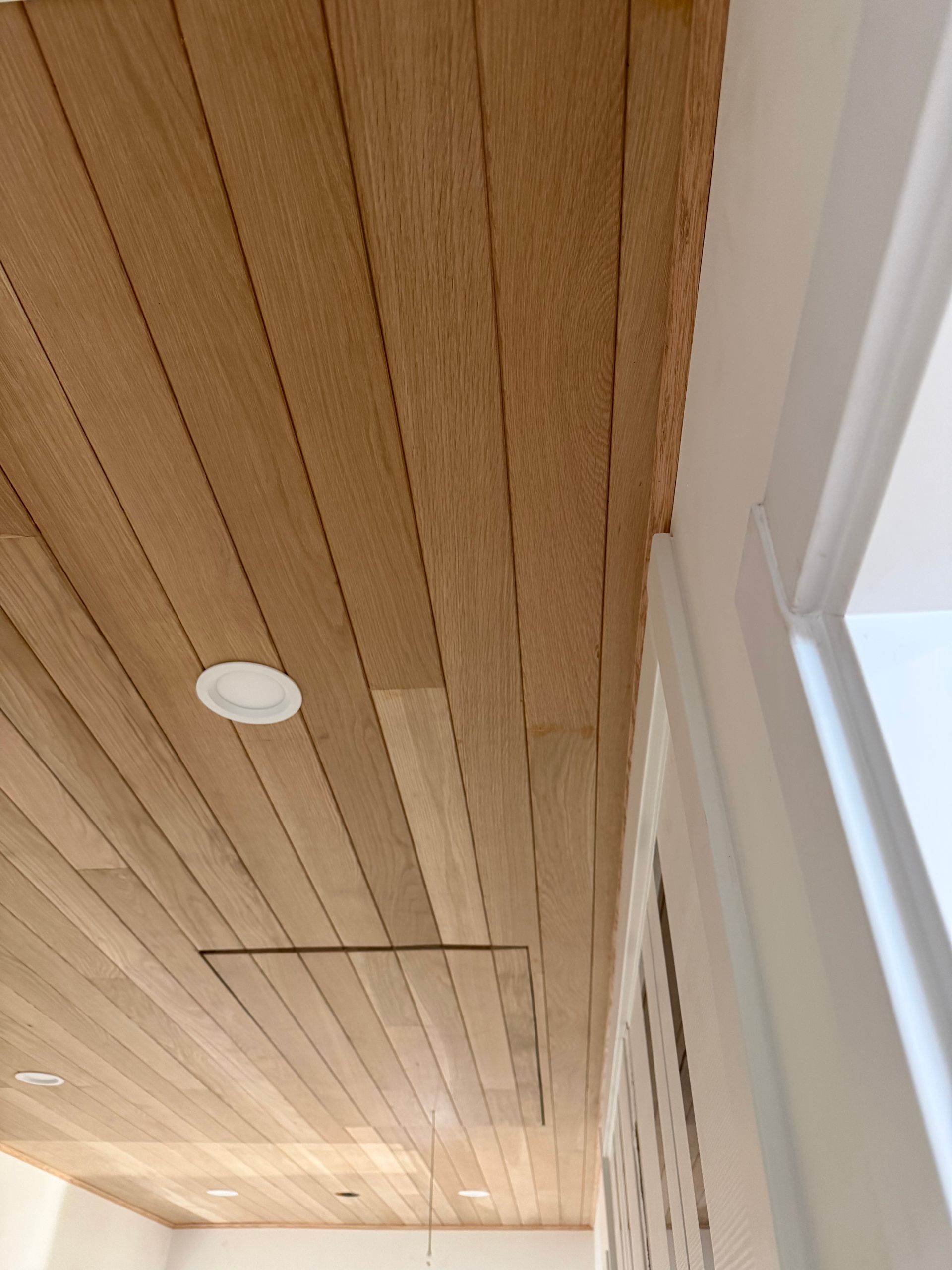 Wood-paneled ceiling with recessed lights beside a white-framed window