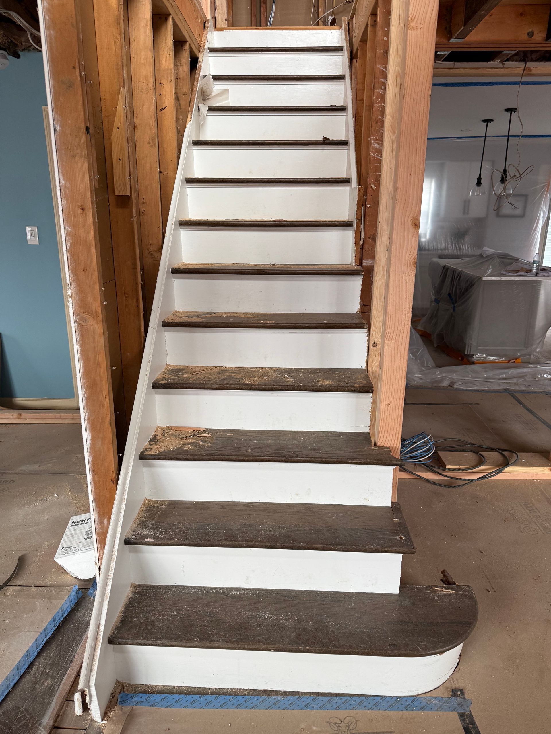 Partially constructed staircase with white steps and exposed wooden framing inside a home renovation