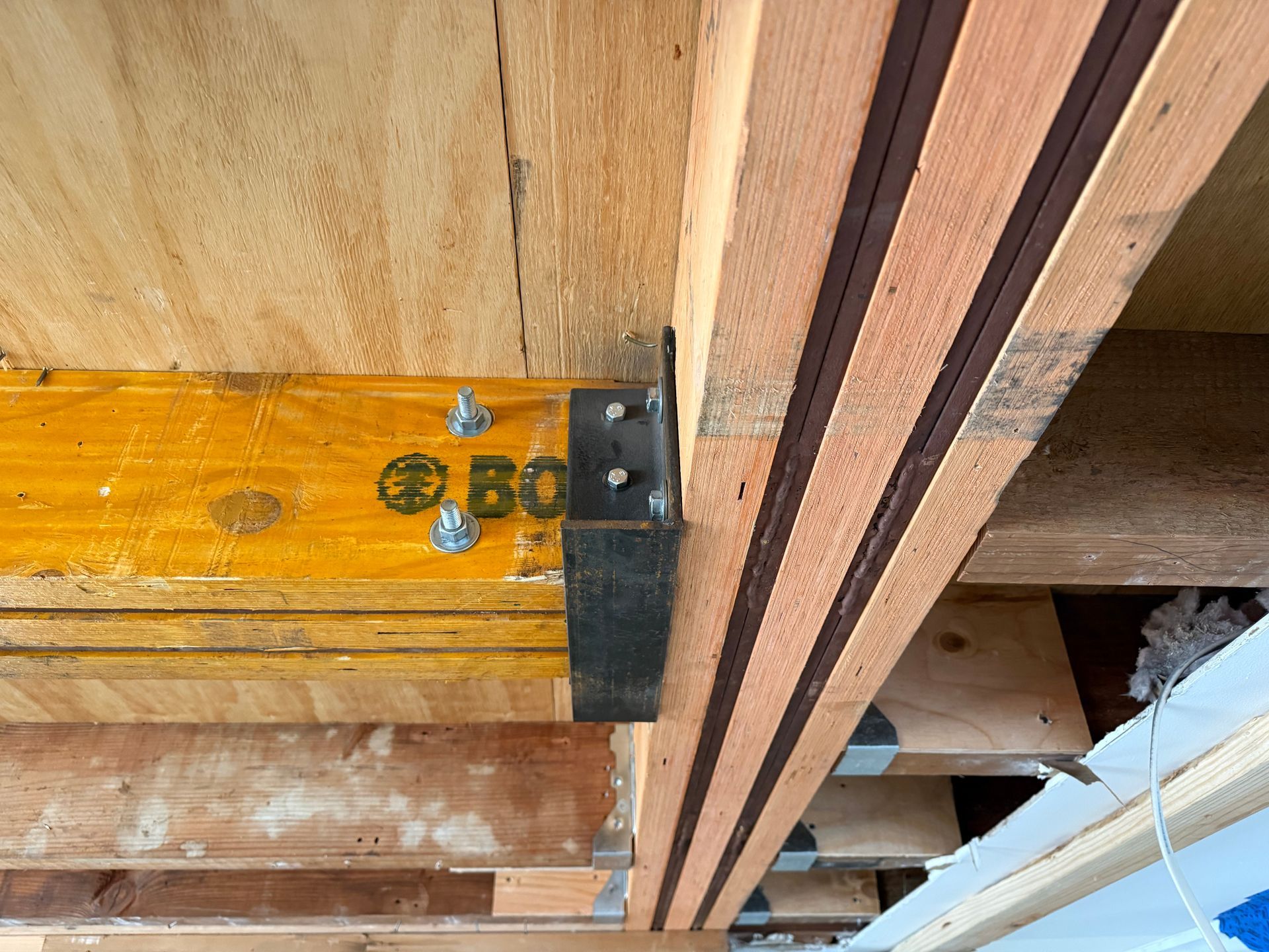 Close-up of wooden beams joined by a black metal bracket with screws and striped wood slats.