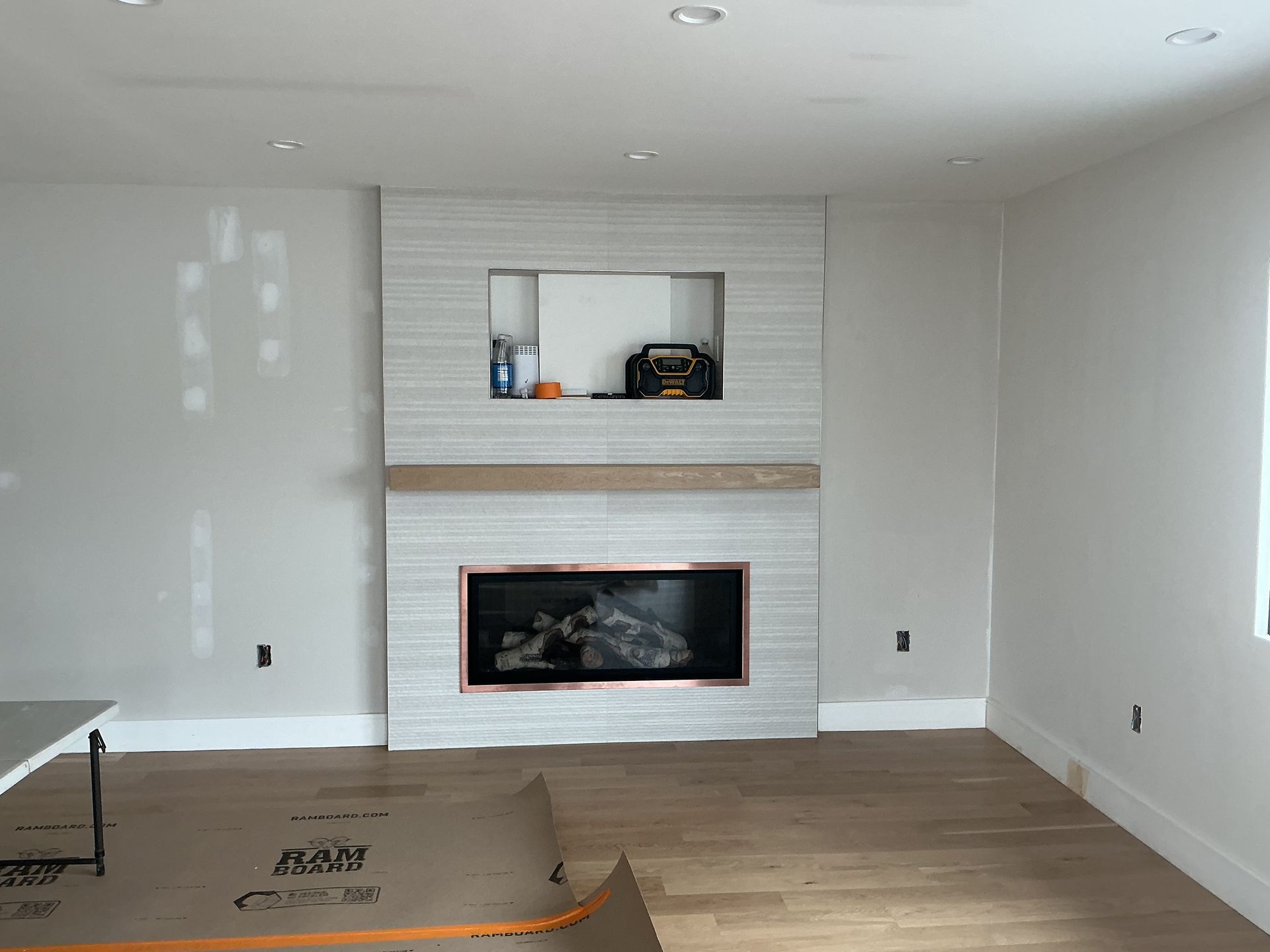 Empty living room with white fireplace, light wood floor, and a small shelf niche above the mantel