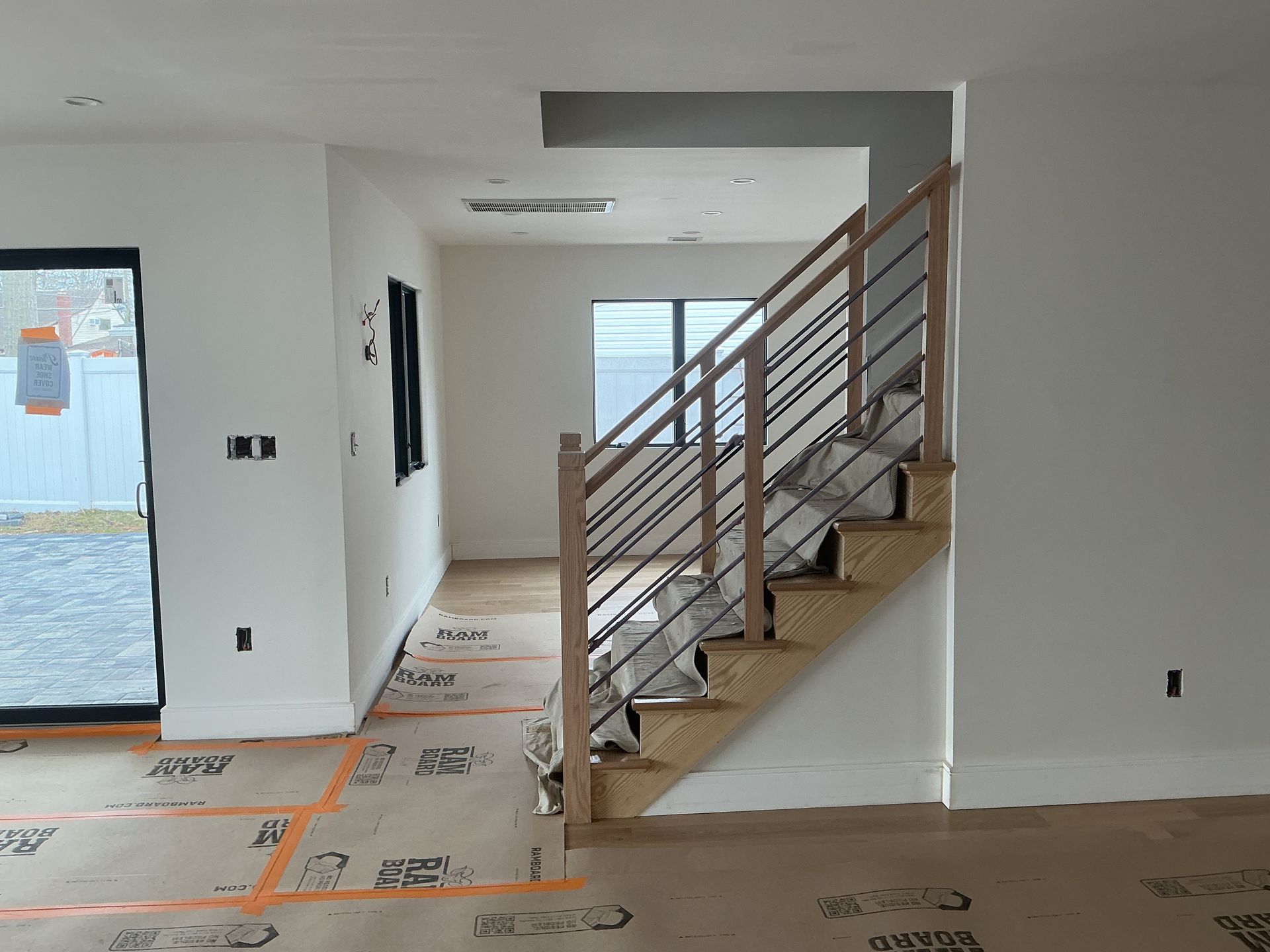 Unfinished interior with staircase, white walls, exposed flooring, and a window at the far end.