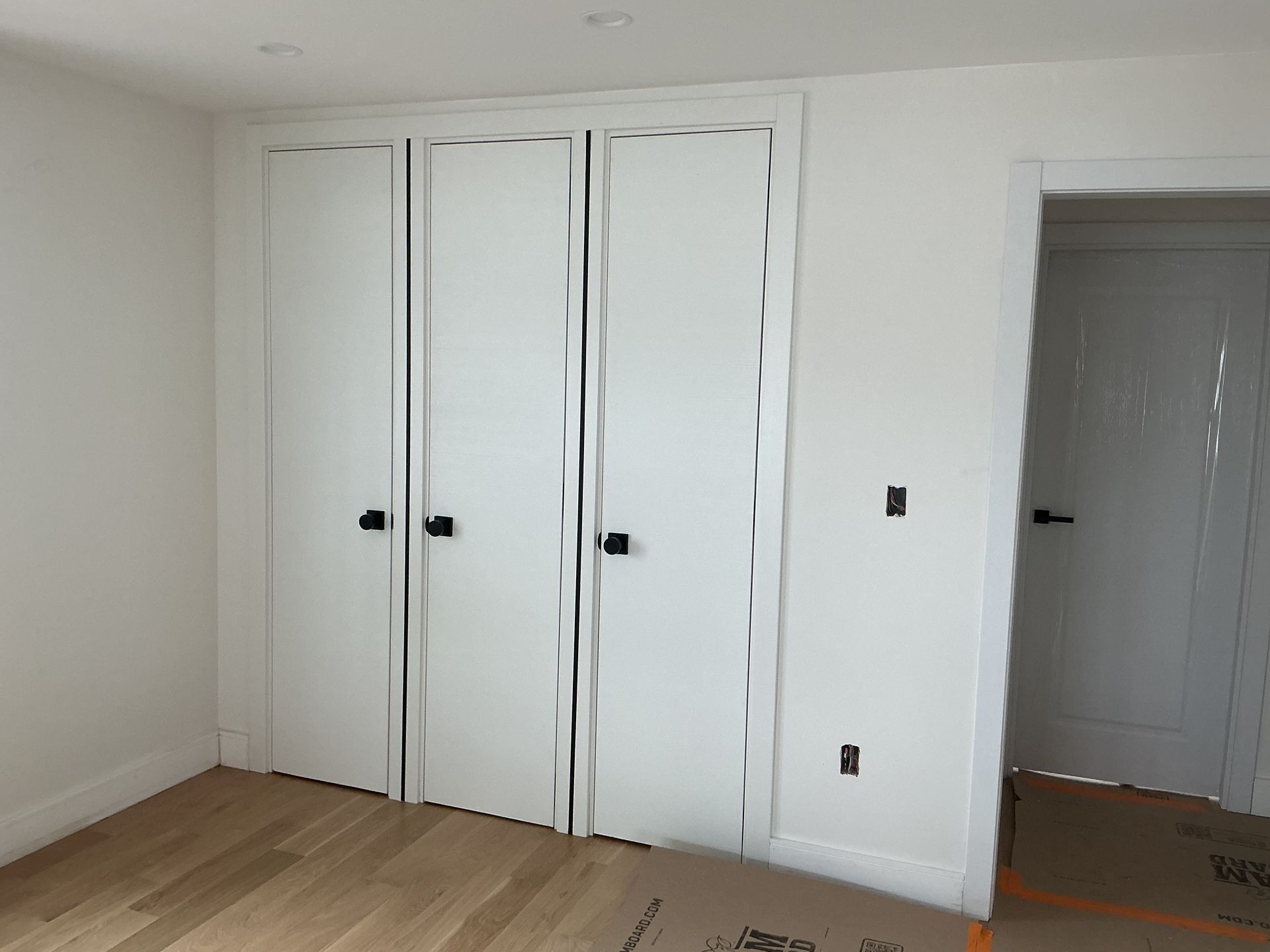 Empty white room with wood floor, built-in closet doors, and an open doorway