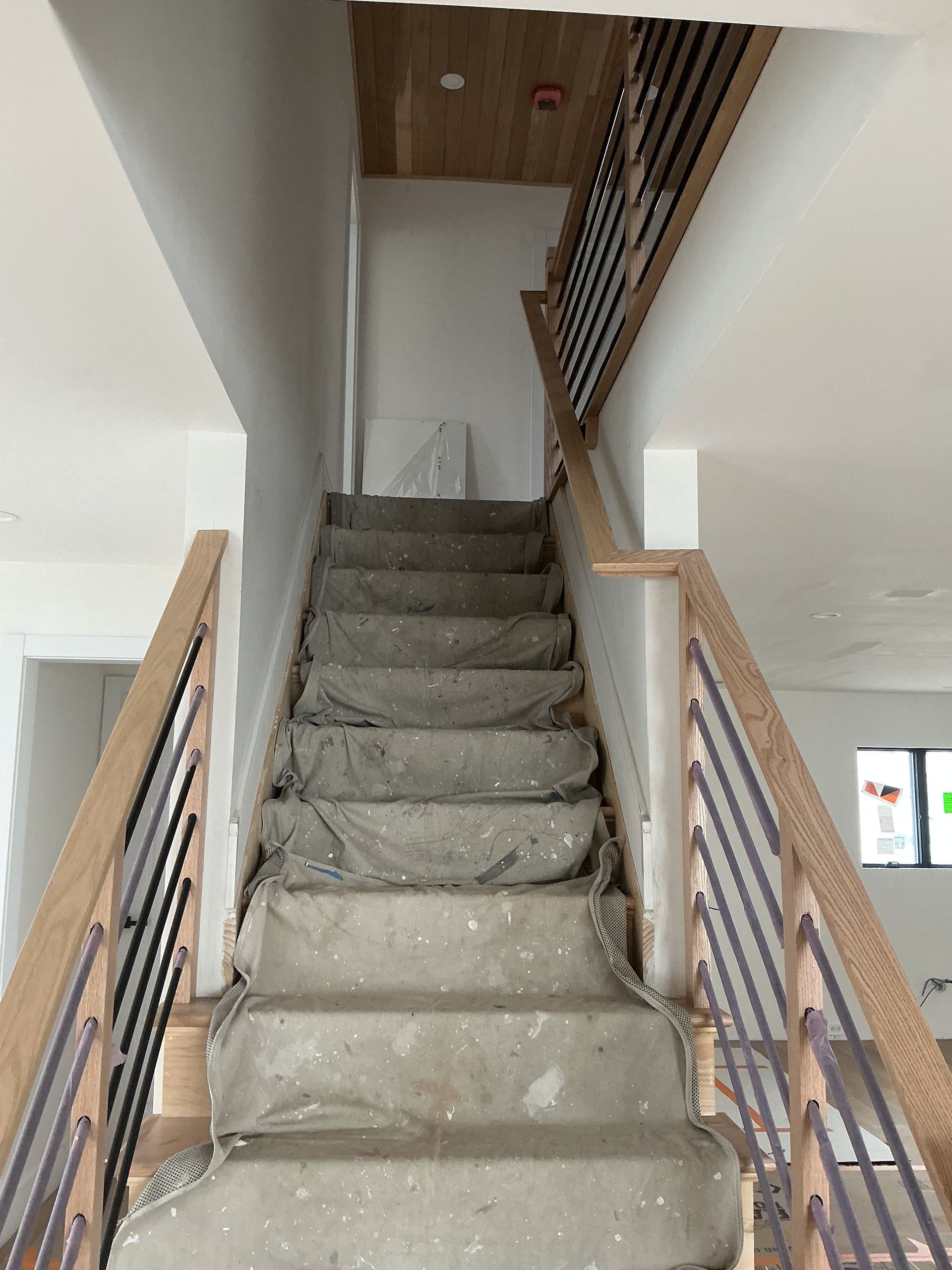 Narrow indoor staircase with gray carpet and wooden railings leading to an upper floor
