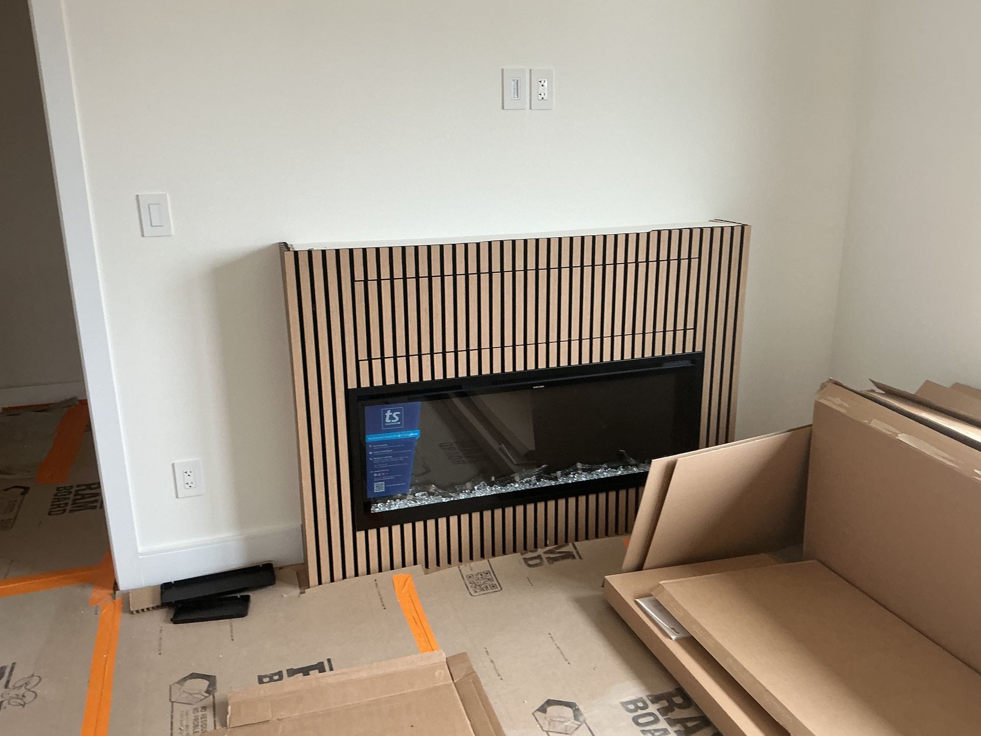 Living room with a modern fireplace wall, striped wood surround, and stacked cardboard boxes.