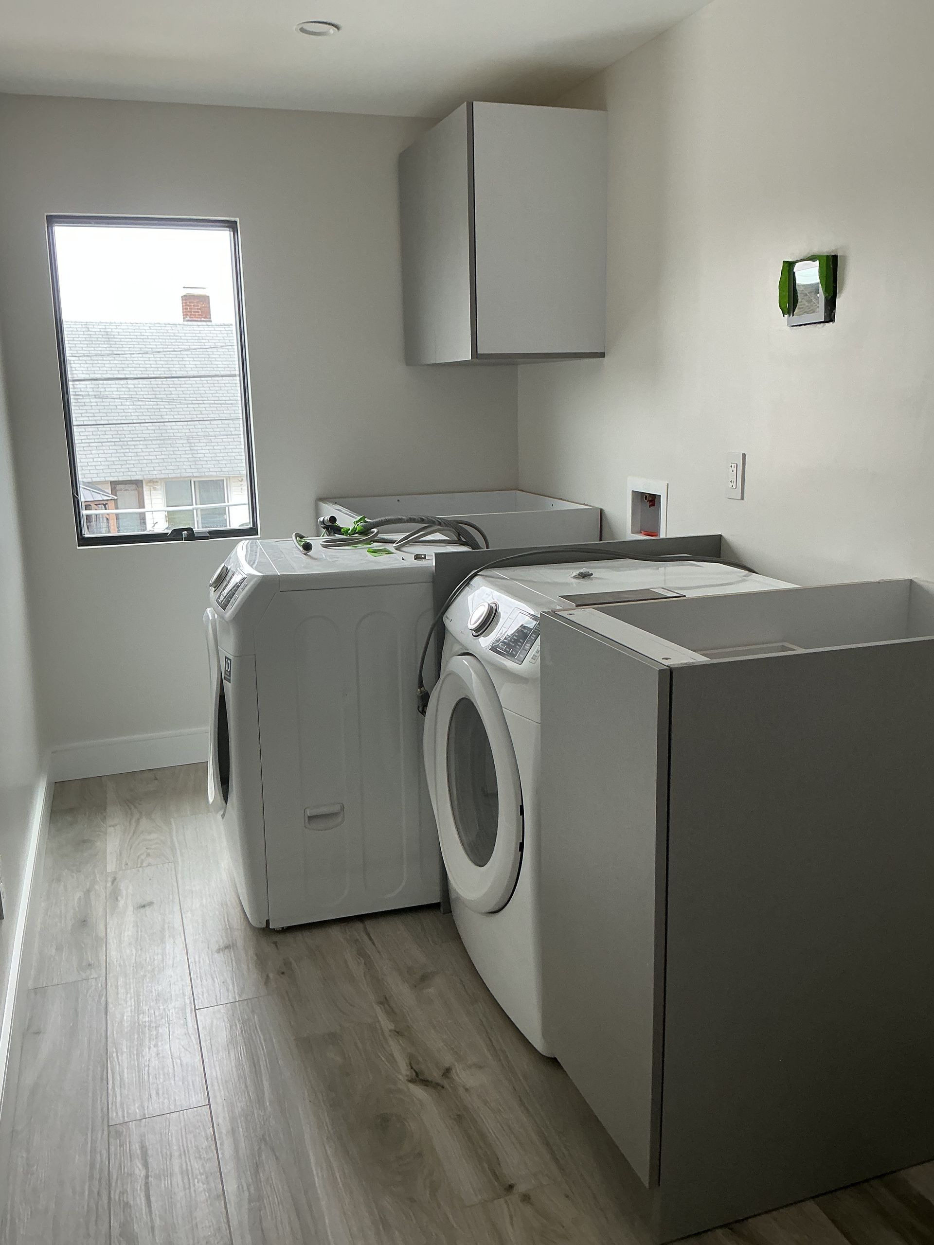 Small laundry room with washer, dryer, utility sink, and cabinets against white walls.