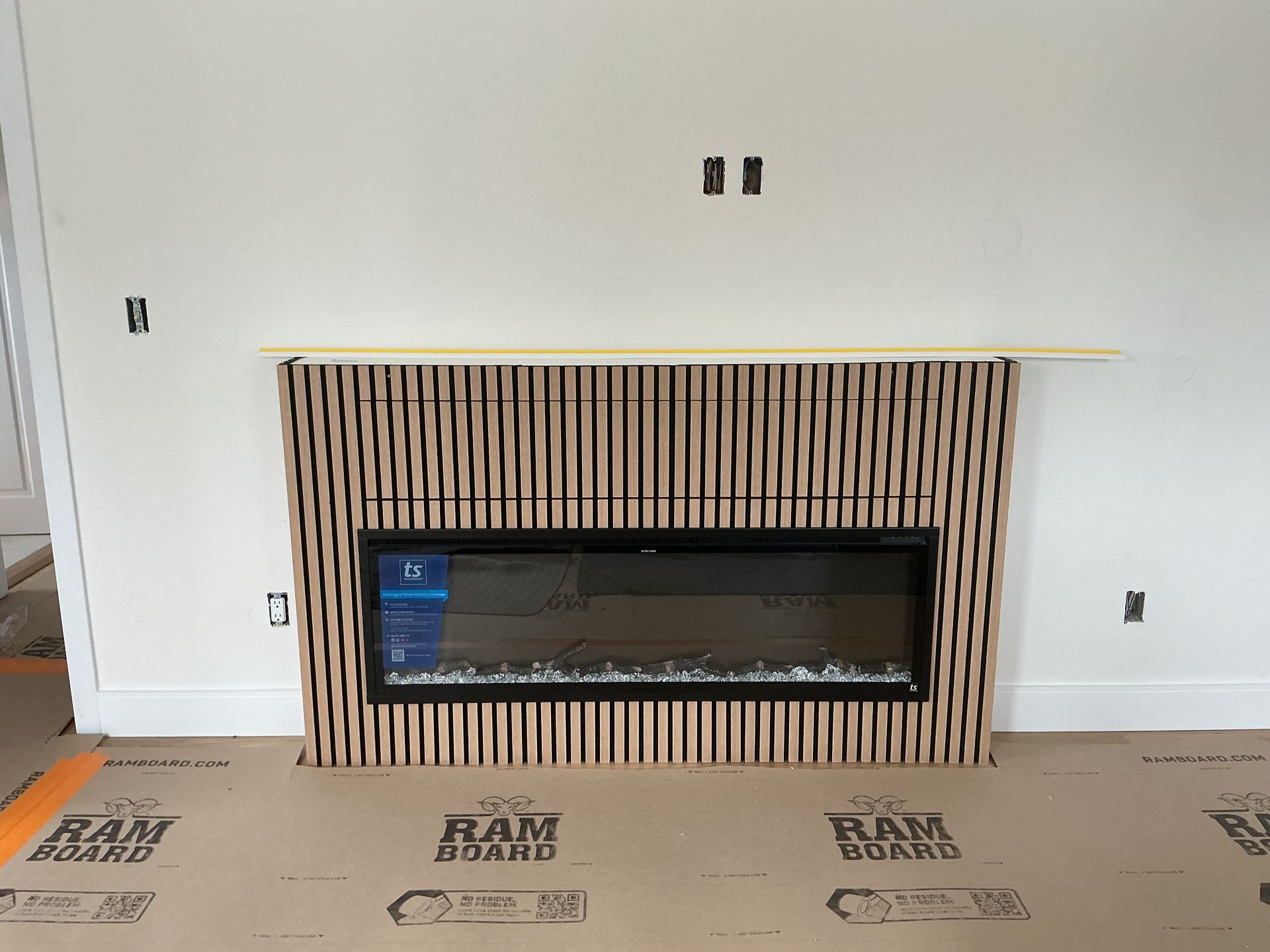 Modern fireplace with vertical wood slats and a stone ledge in a partially finished room