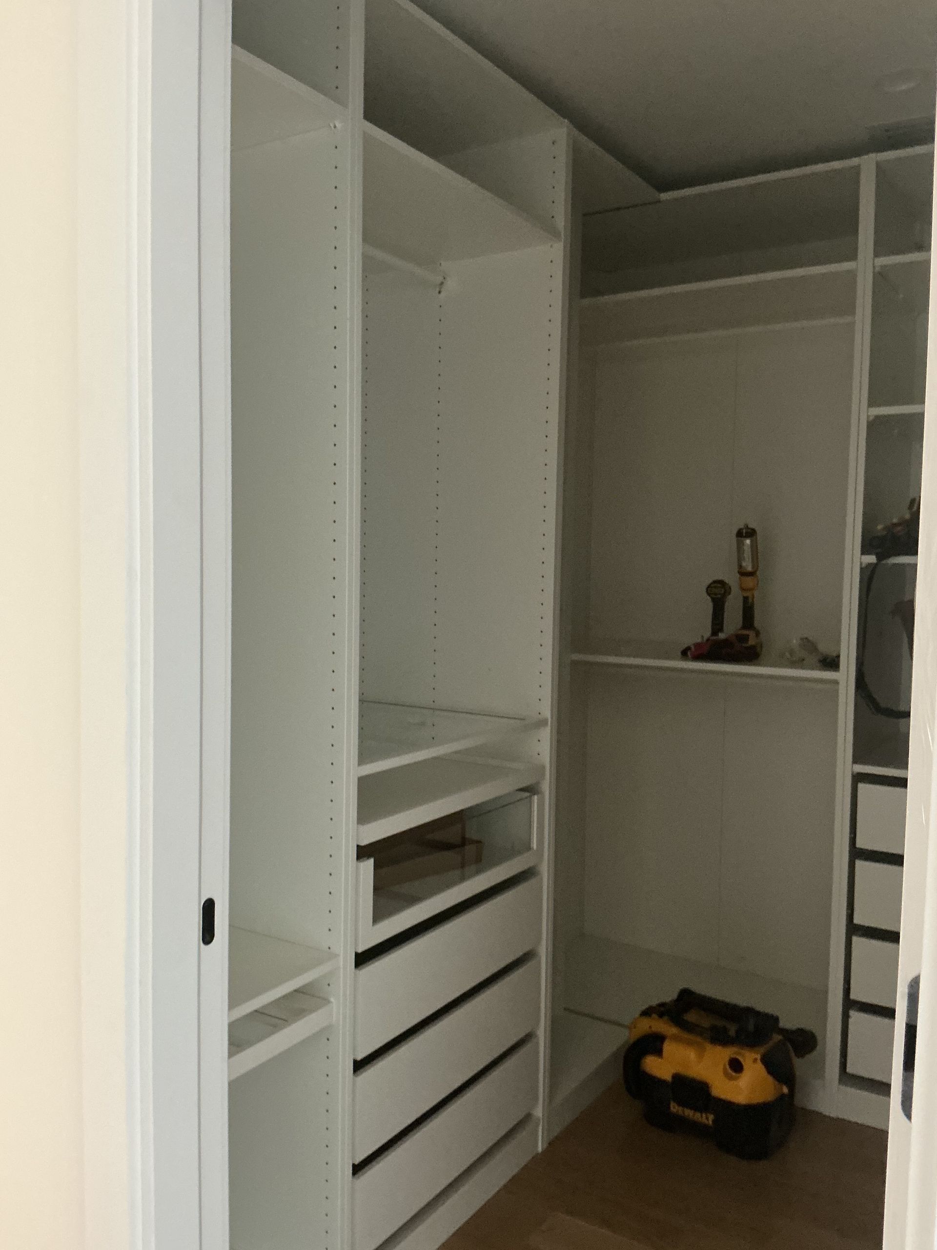 Empty walk-in closet with white built-in shelves, drawers, and a yellow toy truck on the floor
