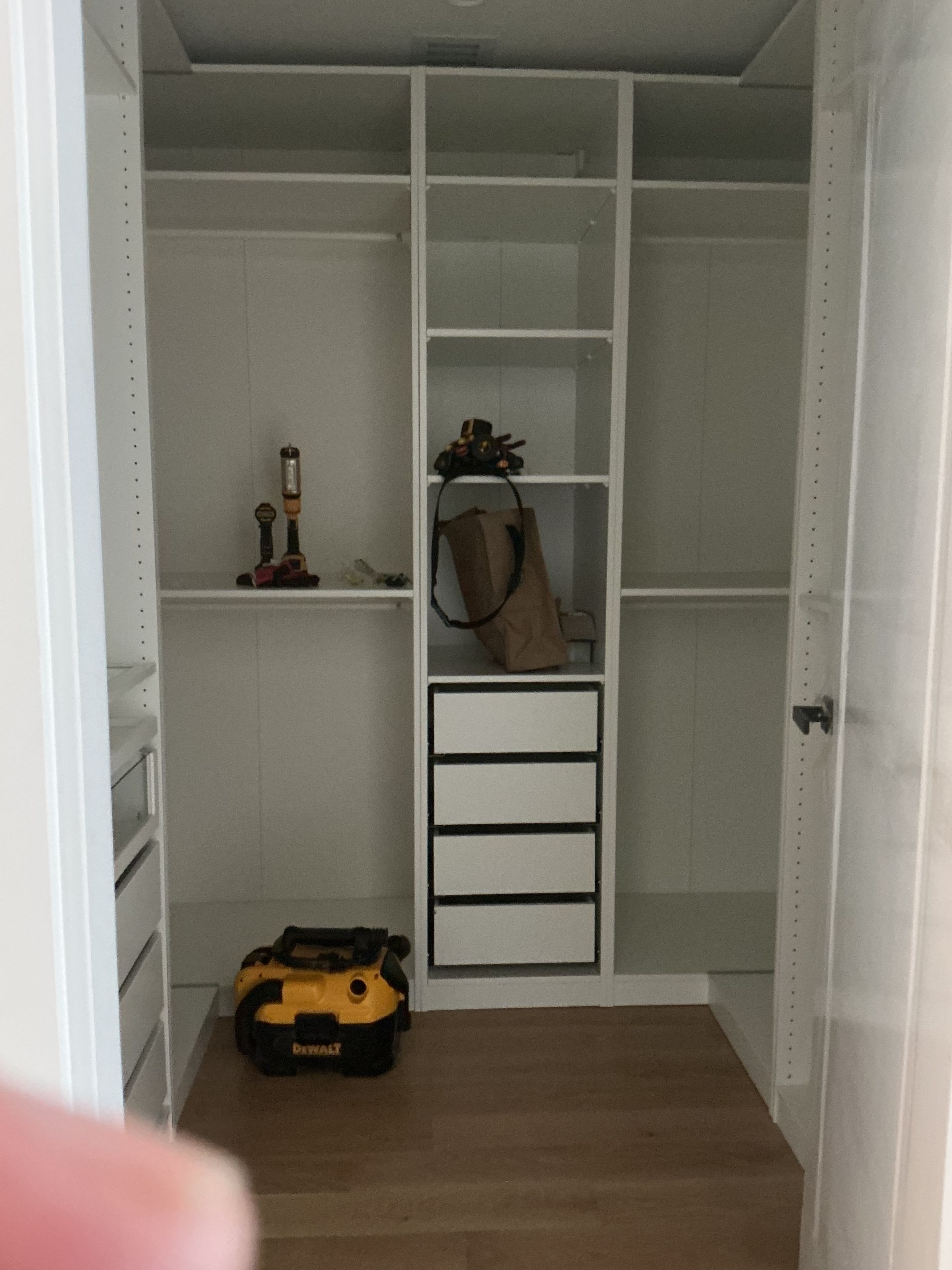 Empty white closet with shelves, drawers, a brown bag, and a yellow toy car on the floor.