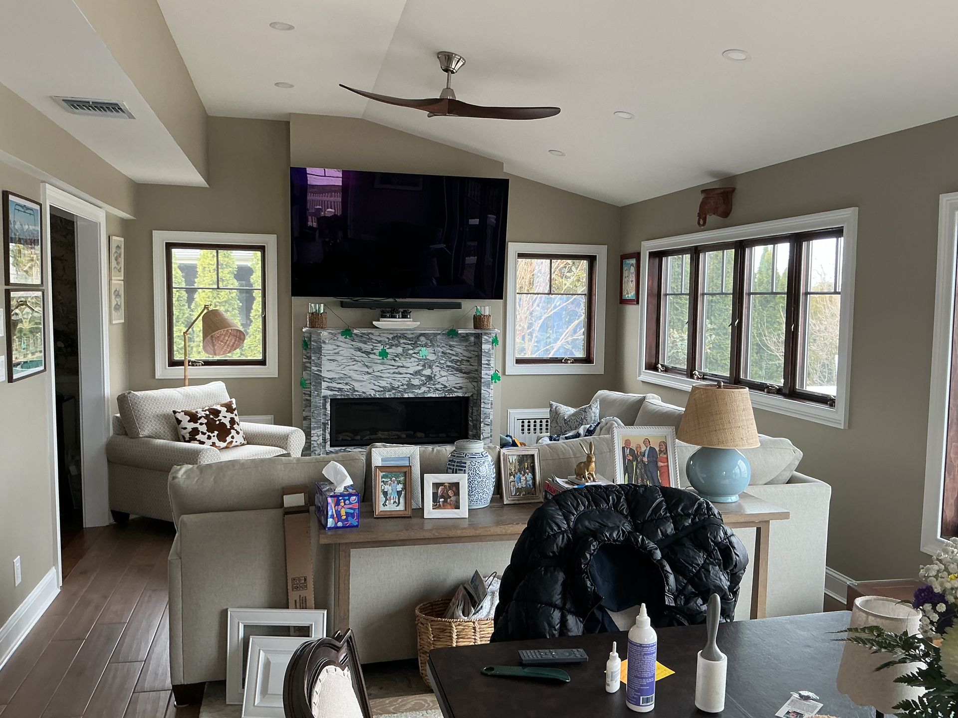 Bright living room with beige sofas, a large TV above a stone fireplace, and many windows letting in light.