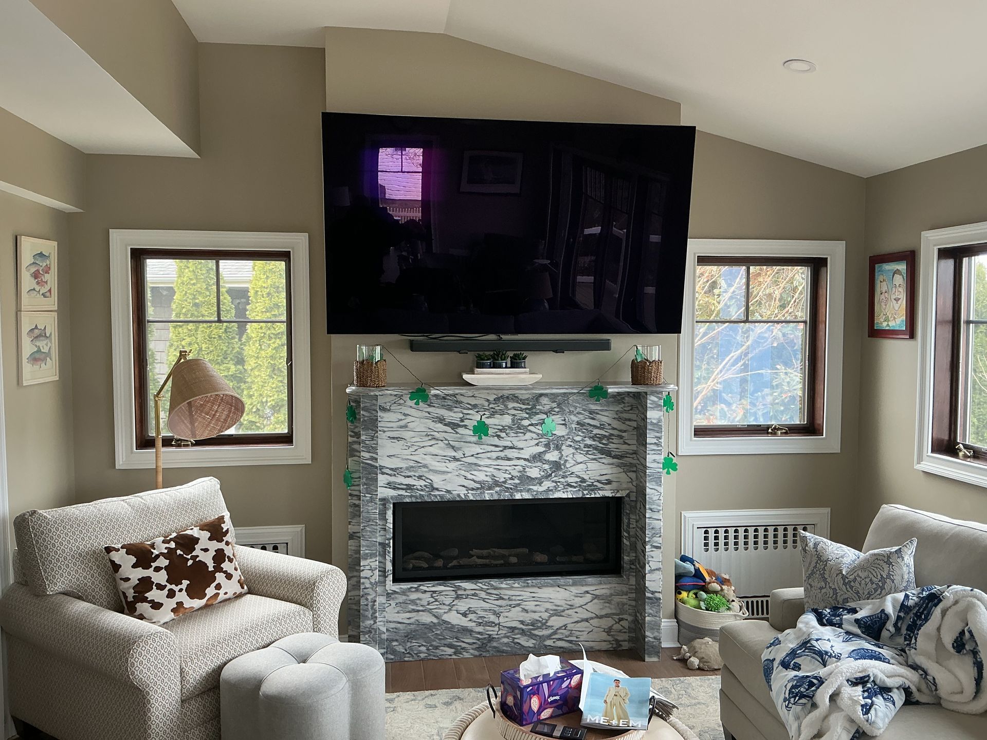 Cozy living room with fireplace, large TV, armchair, windows, and a pile of blankets on the floor