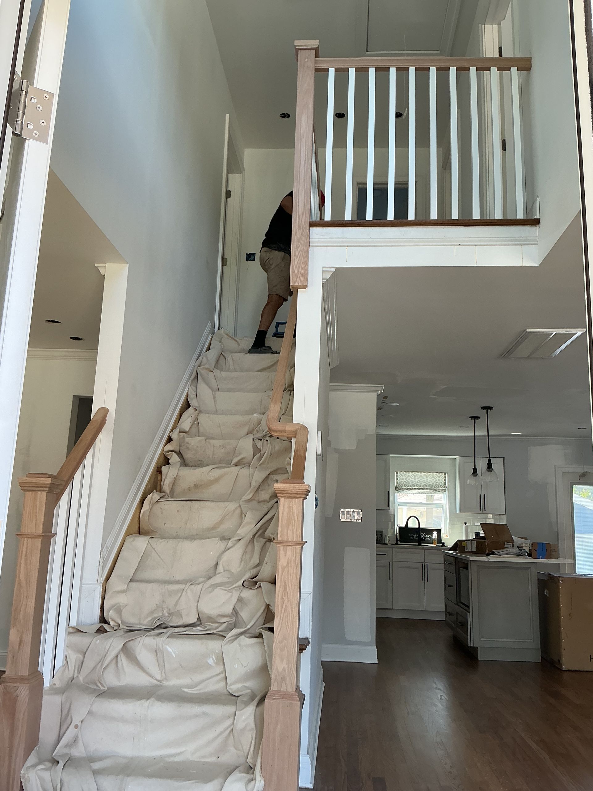Interior of a house with a steep staircase under renovation, covered in protective sheeting, beside an open living area.