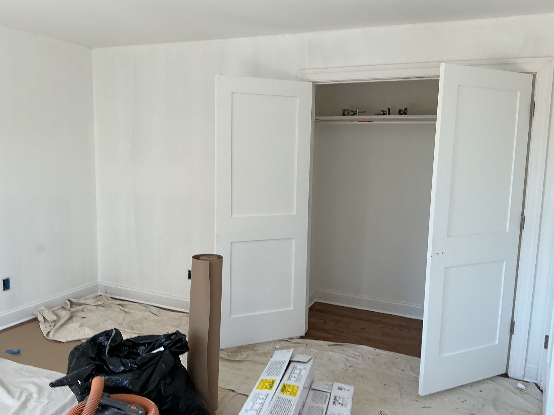 Bedroom with open closet doors, white walls, and construction materials on the floor.