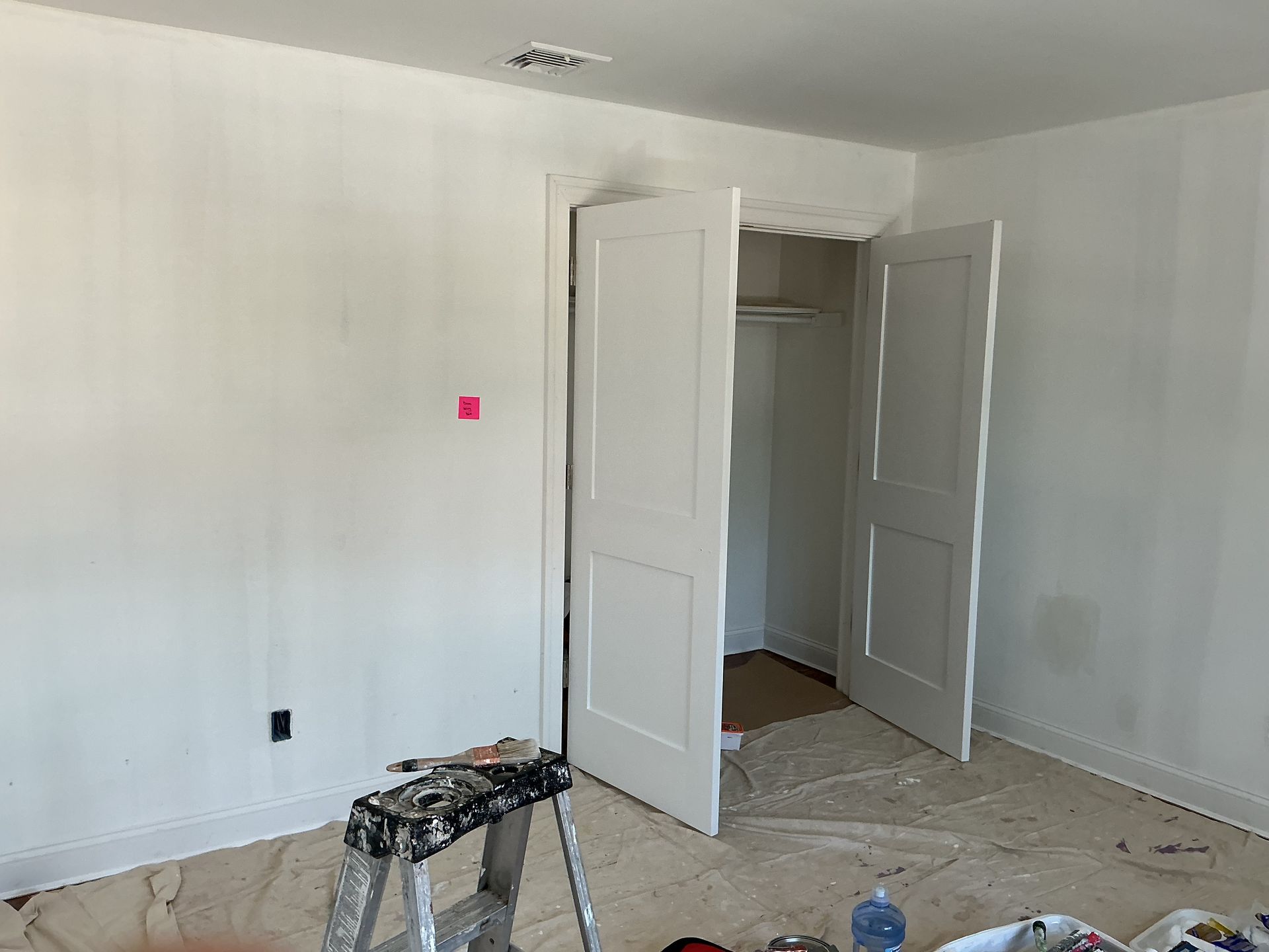 Empty white room with open closet doors, paint tools, and renovation debris on the floor