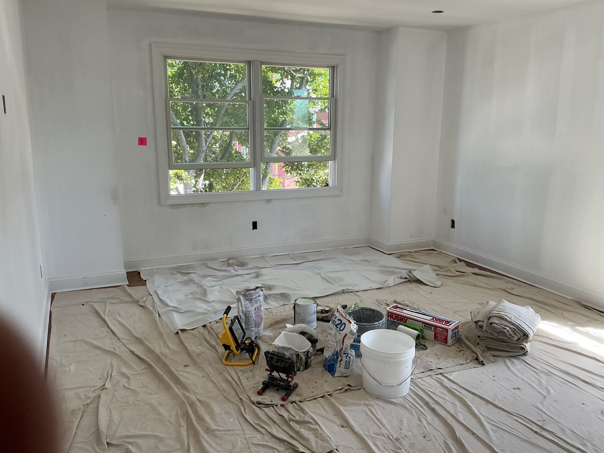 Bright room under renovation with a window, paint supplies, and drop cloths on the floor