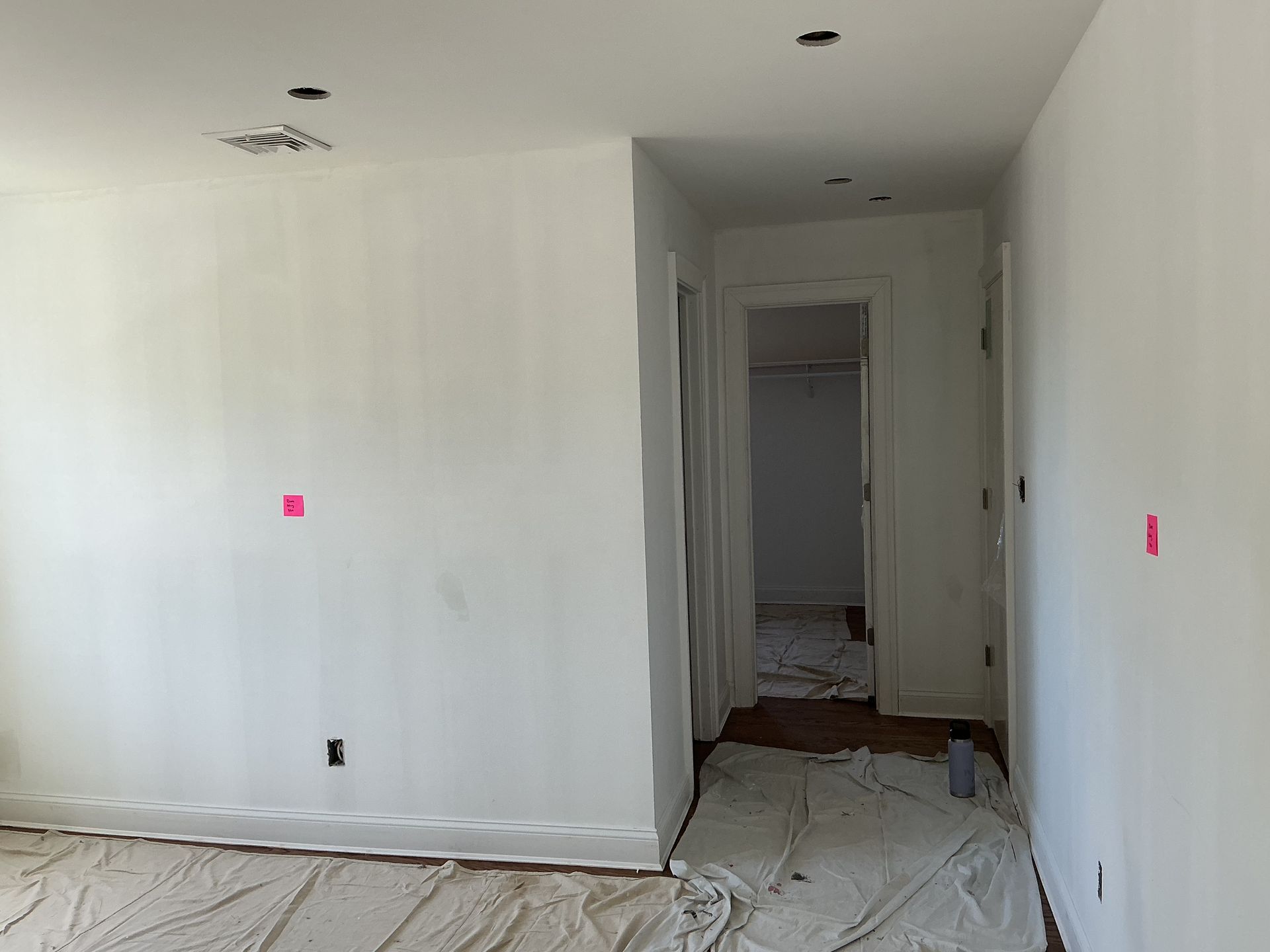 Empty white hallway with unfinished flooring and exposed ceiling lights leading to a doorway