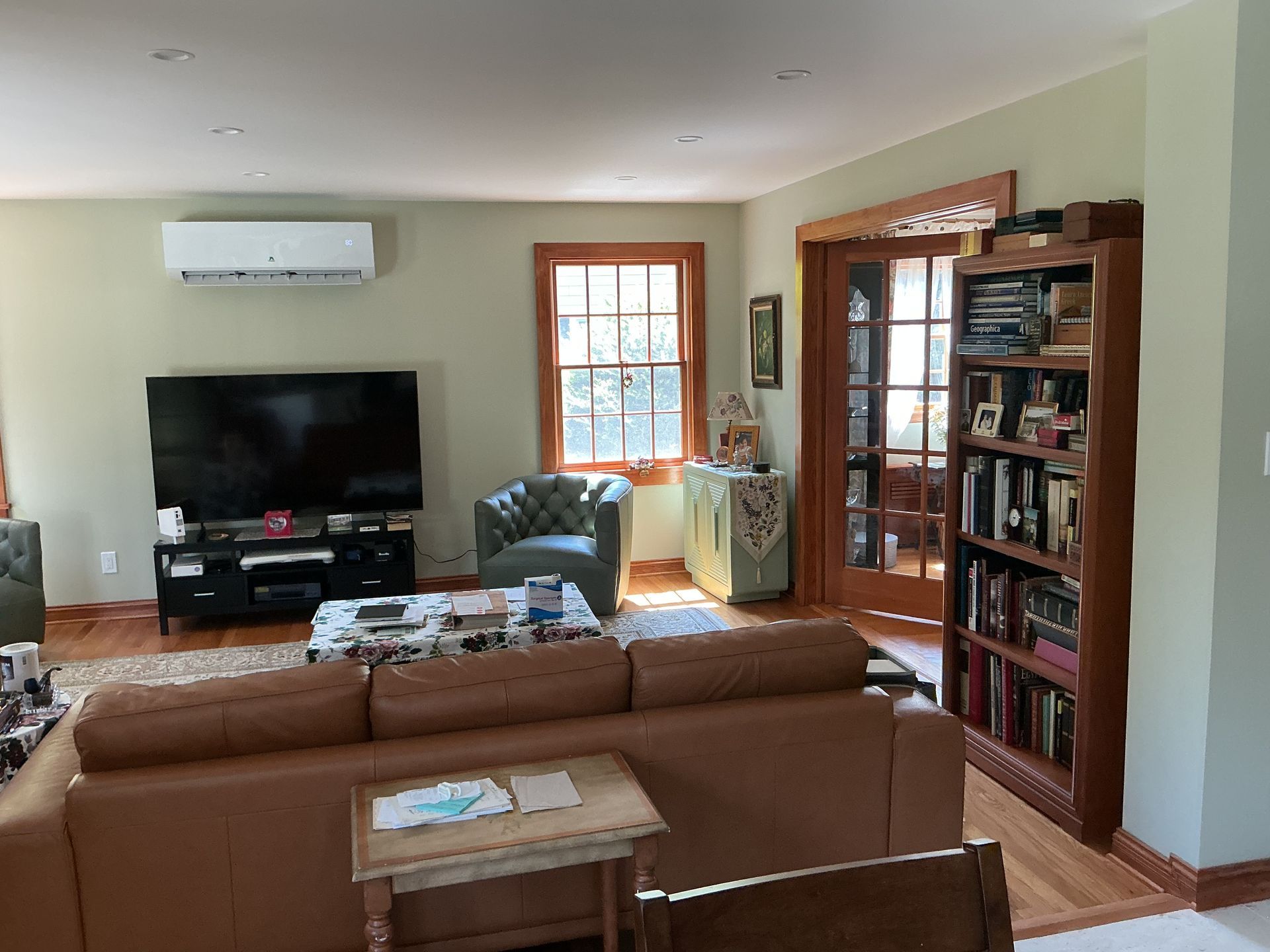 Living room with brown sofa, TV, green chair, window, and bookshelf against light walls
