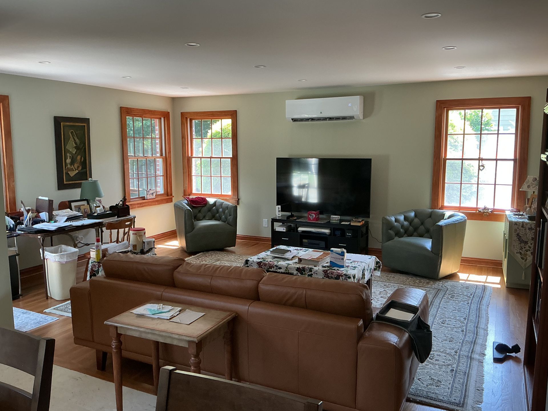 Bright living room with brown sofas, TV, windows, and wall-mounted air conditioner