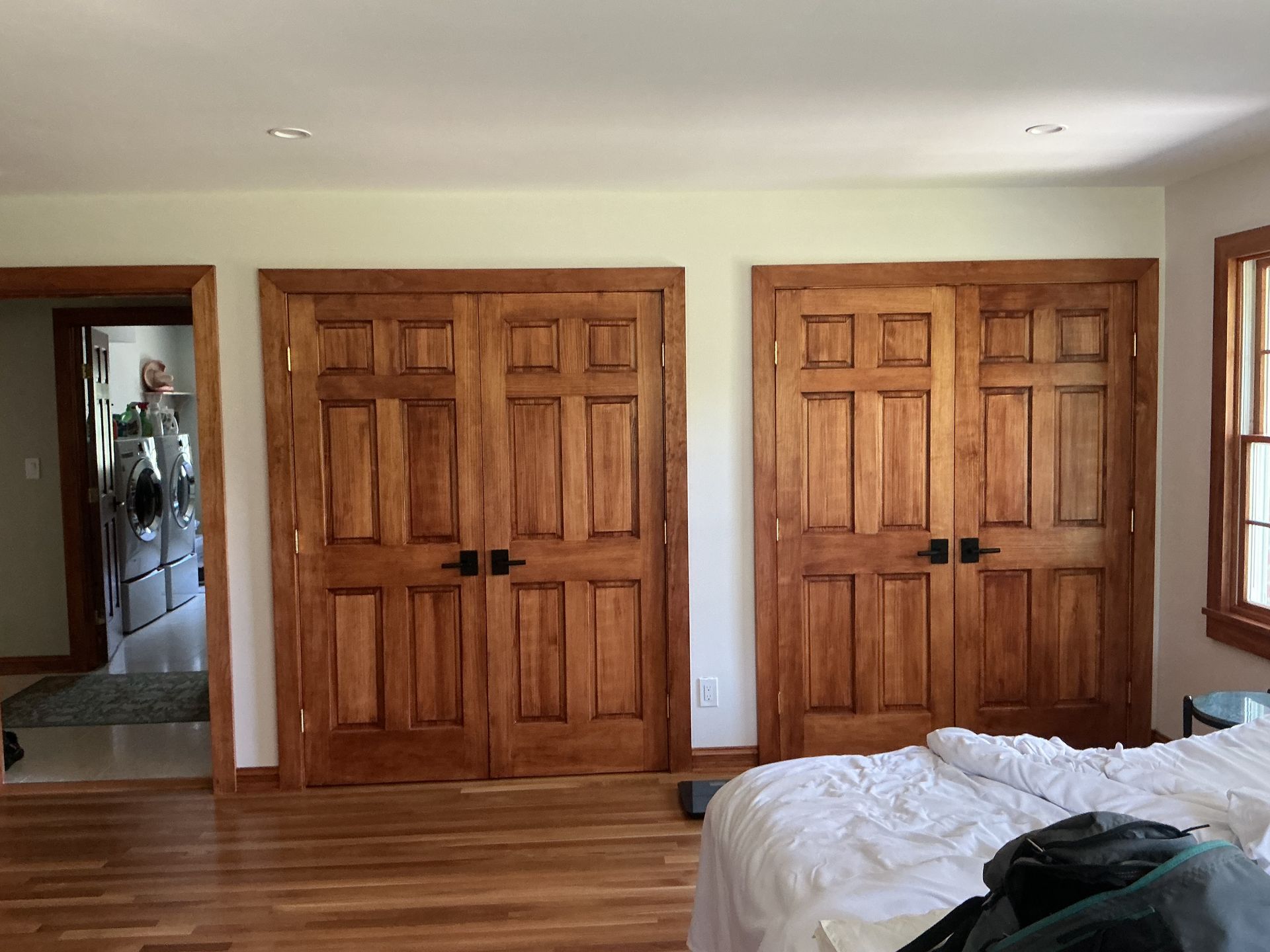 Bedroom with two wooden double closets, a mirrored doorway, and part of a bed in the foreground.