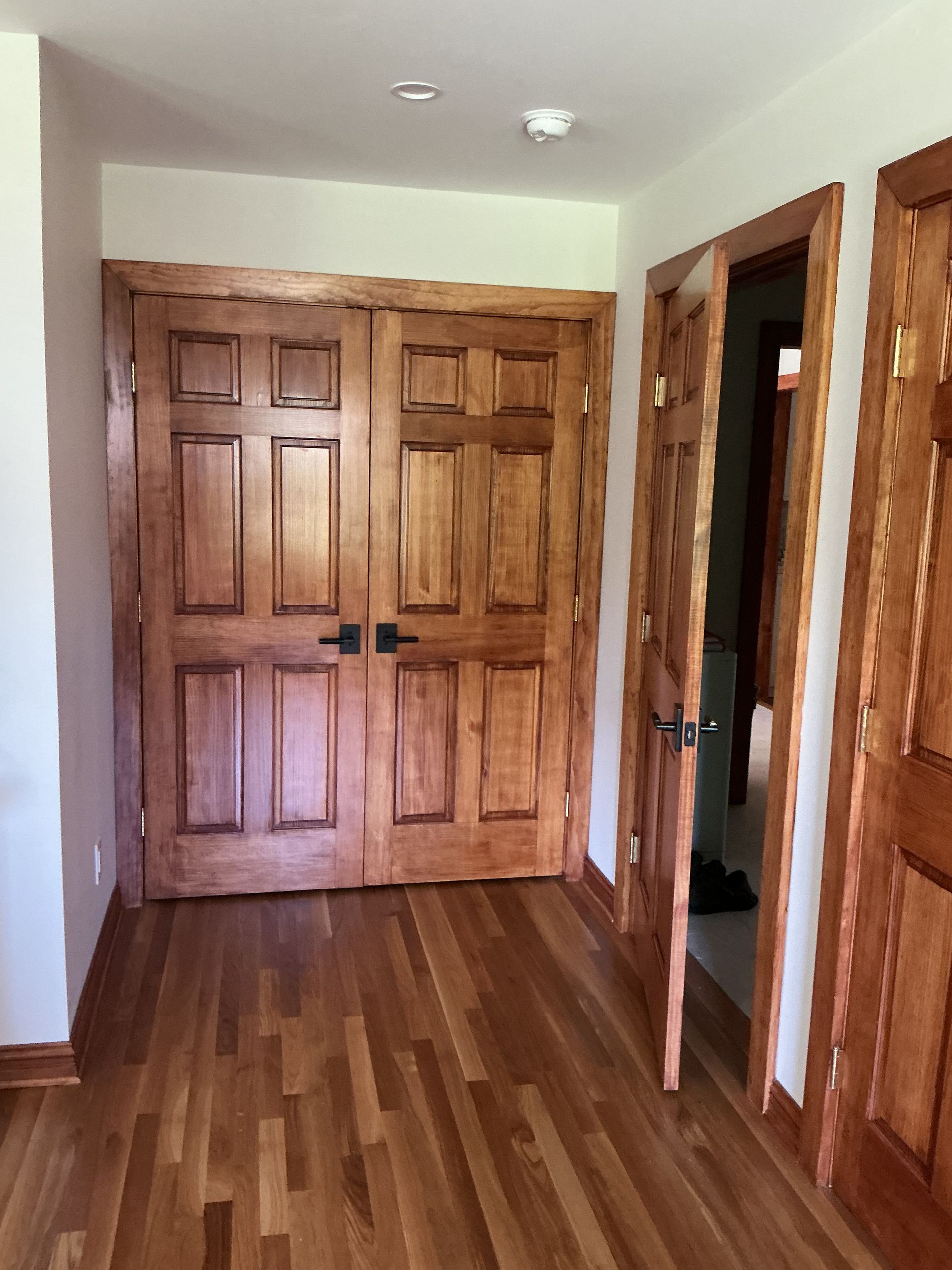Wooden hallway with closed double doors, wood floors, and open closet doors on the right