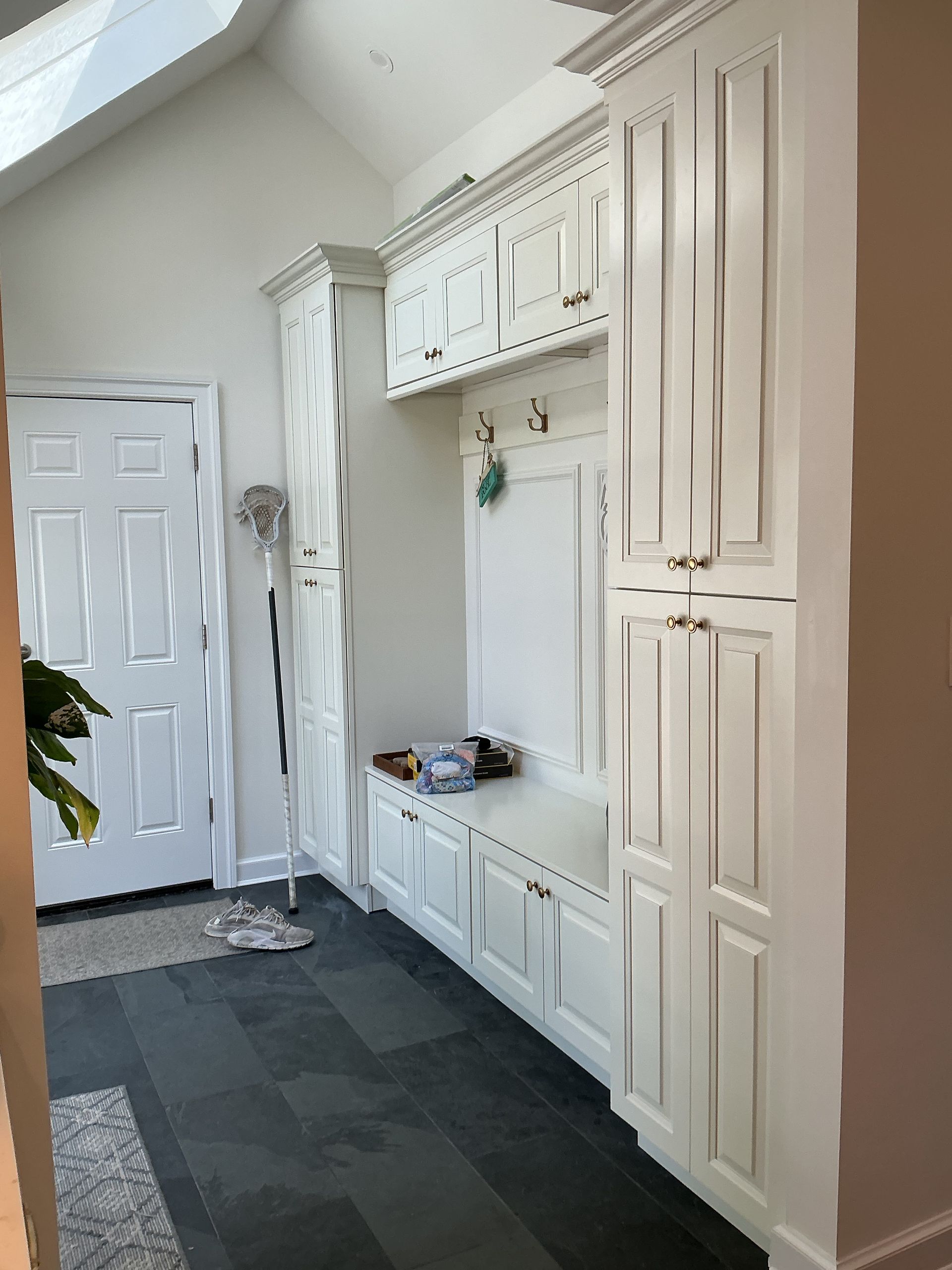Bright hallway with white built-in cabinets, coat hooks, and a dark runner rug near a front door.