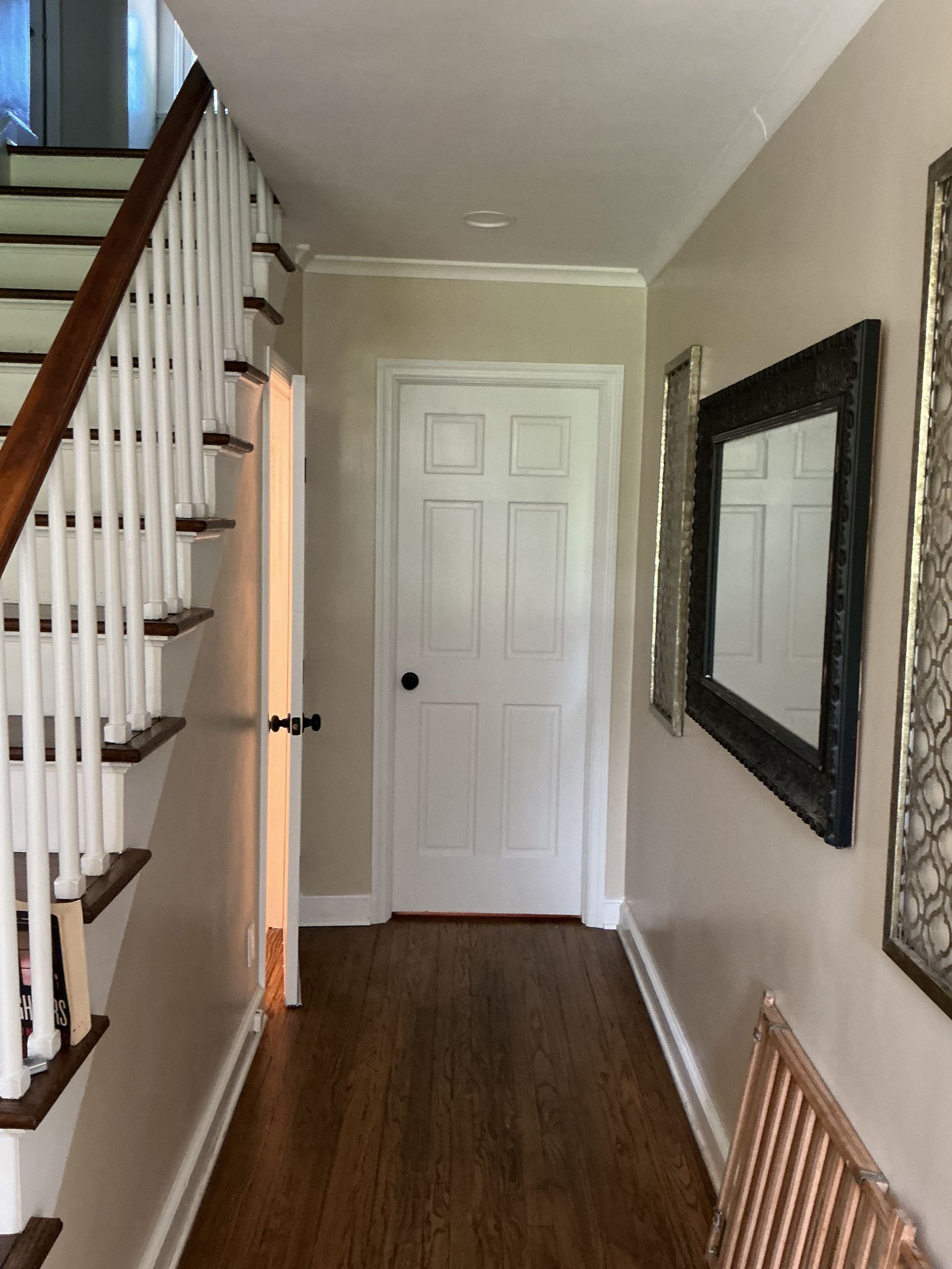 Narrow hallway with stairs, white doors, wood floor, wall mirror, and a radiator cover.