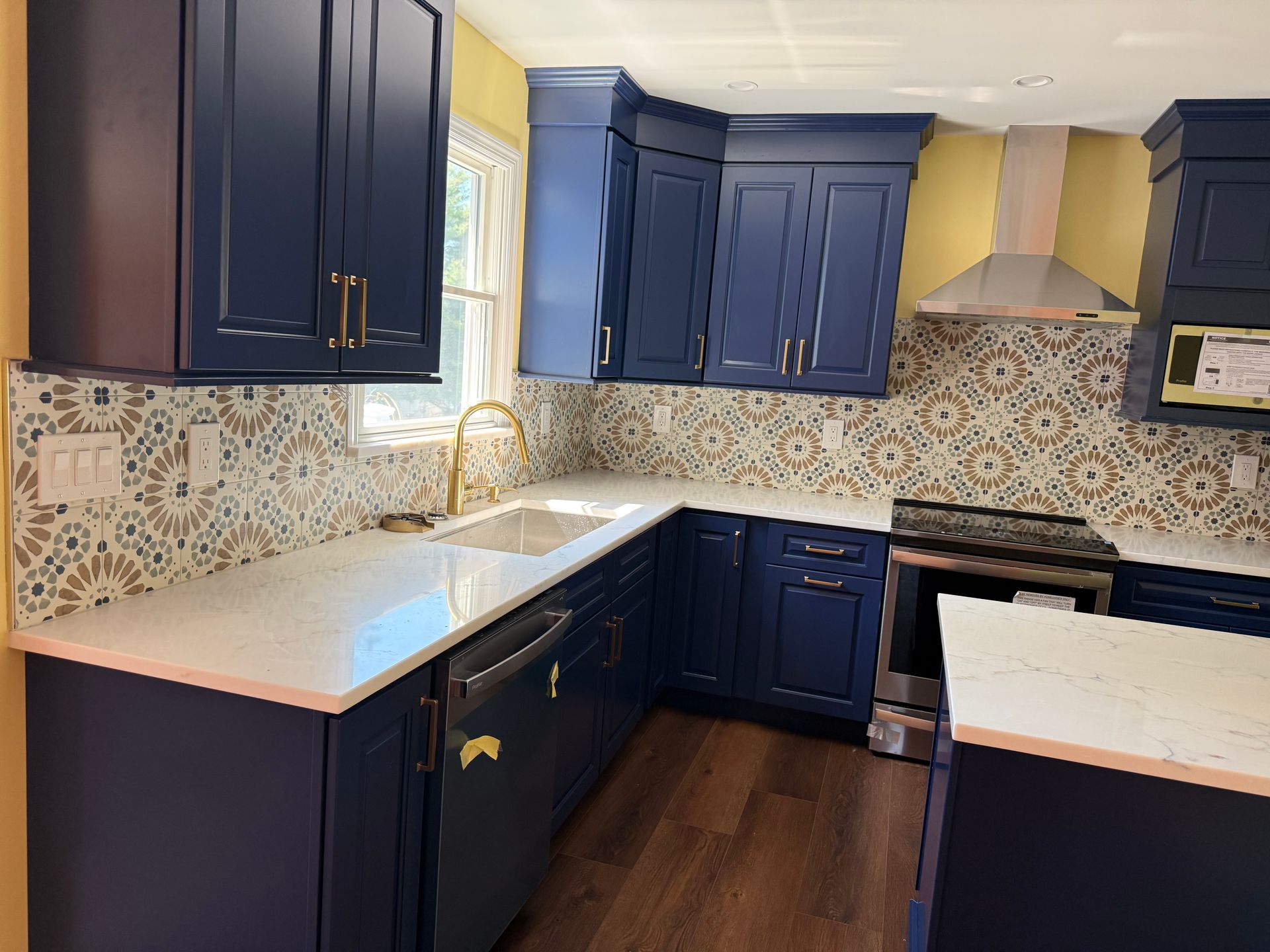 Compact kitchen with dark blue cabinets, white countertops, patterned backsplash, and stainless steel stove.