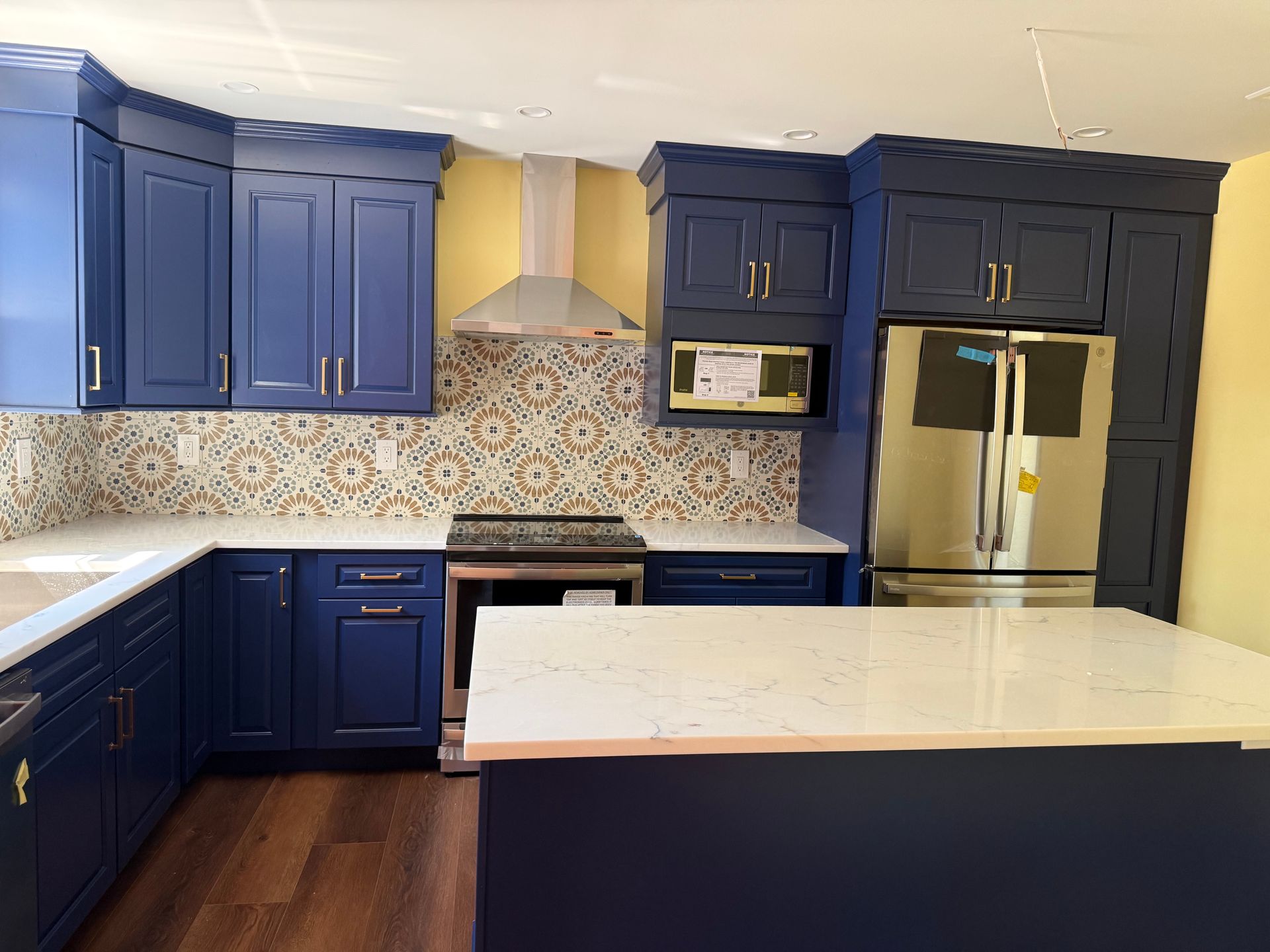Modern kitchen with navy cabinets, patterned backsplash, stainless appliances, and a large white island.