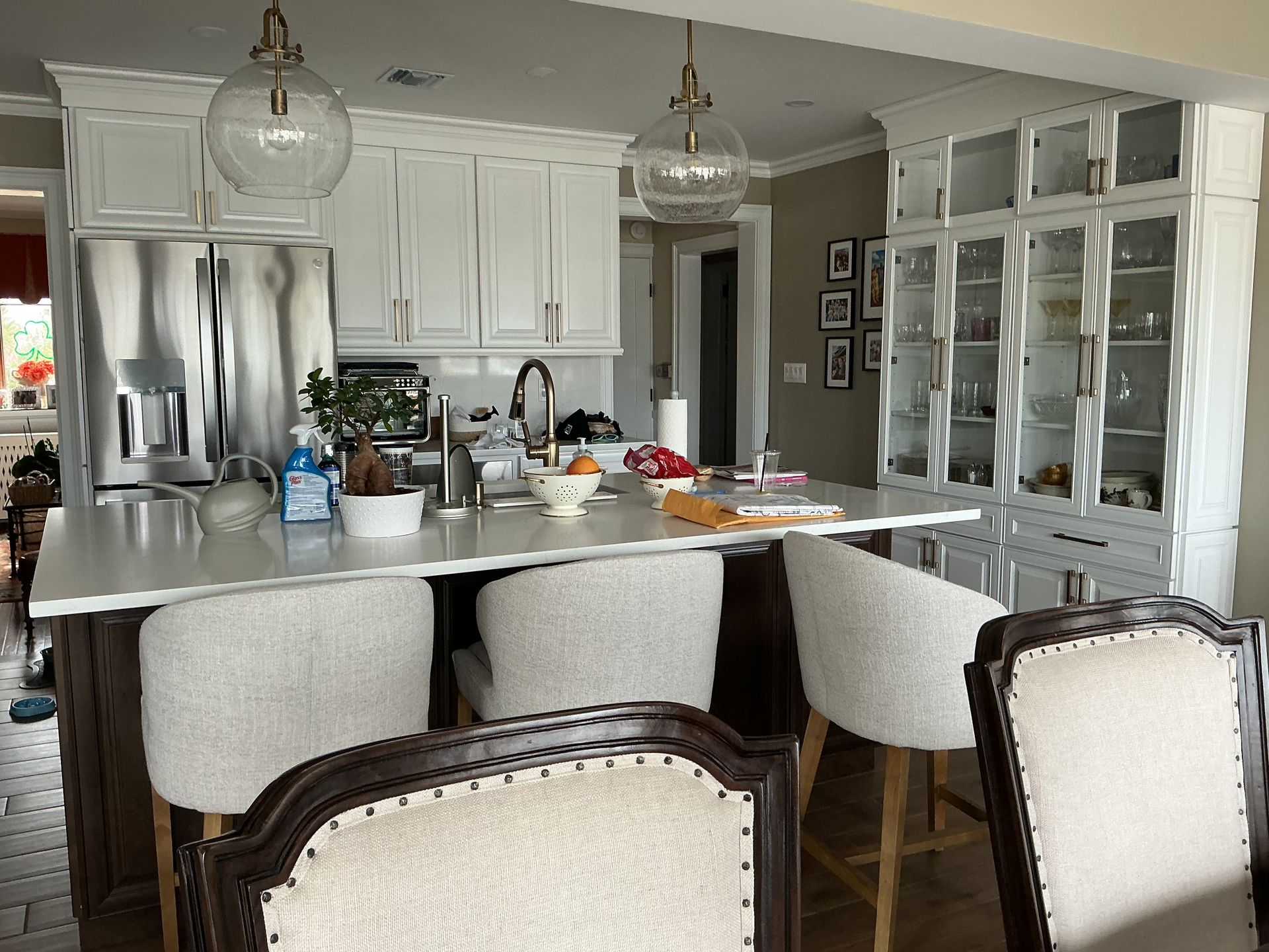 Modern kitchen with white cabinets, stainless fridge, large island, pendant lights, and woven bar stools.