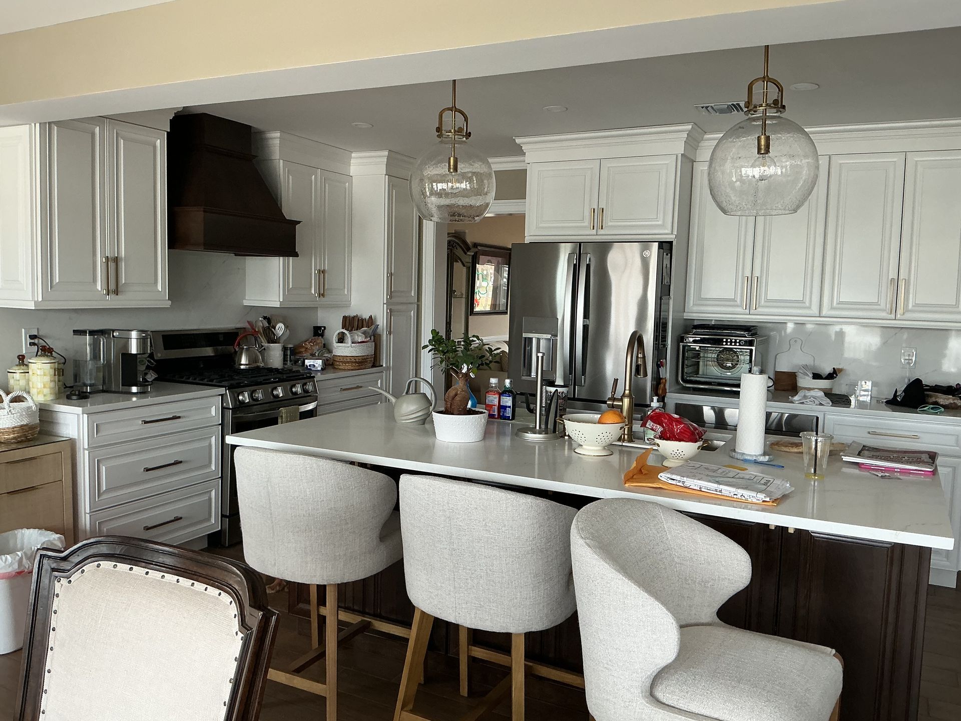 Modern white kitchen with island, stainless steel appliances, and three upholstered barstools