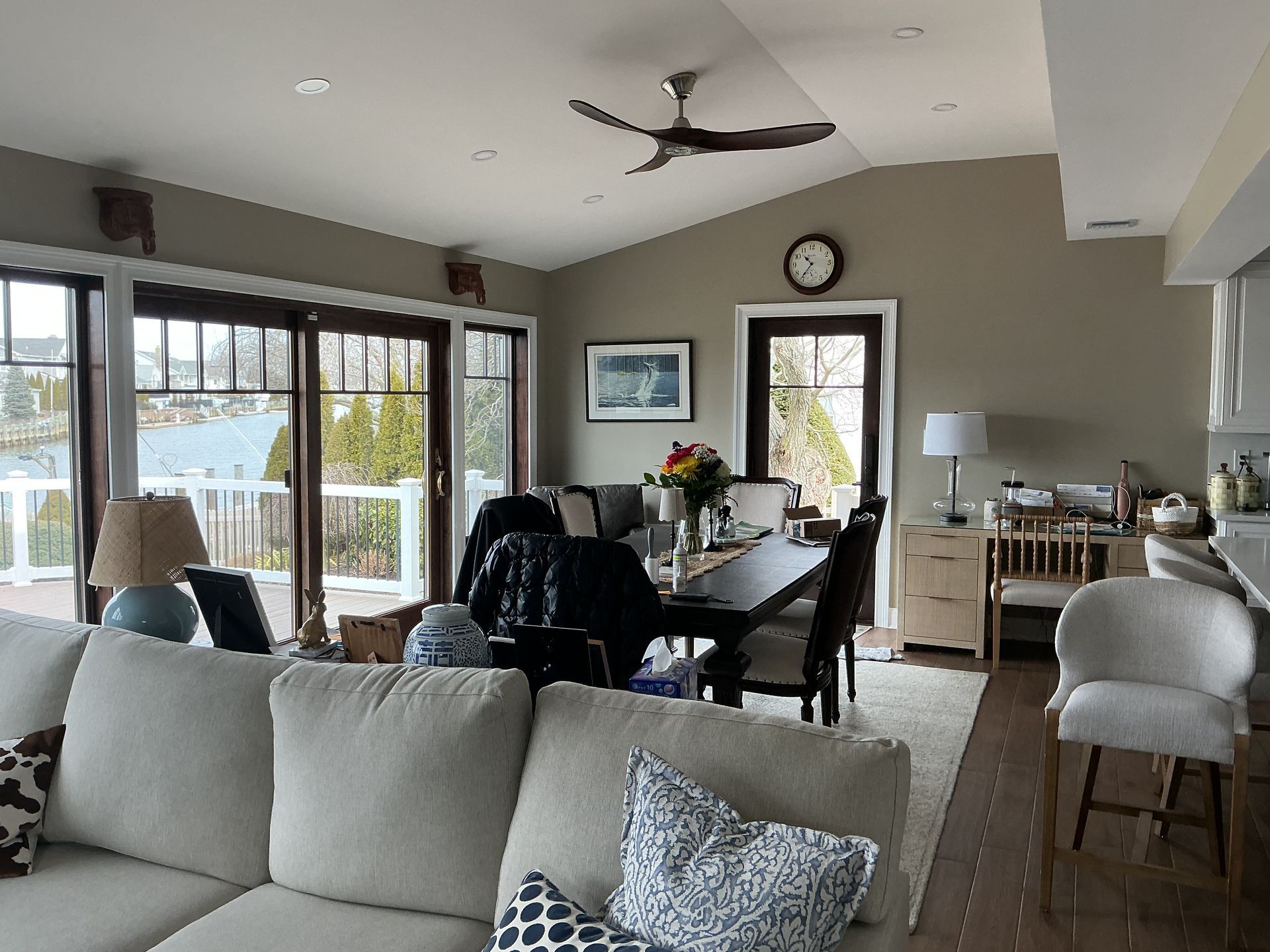 Bright open living-dining room with large windows, gray sofa, dining table, and ceiling fan