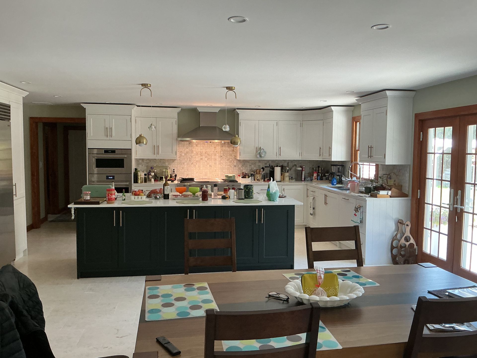 Open kitchen and dining room with dark island, white cabinets, and wood-framed glass doors