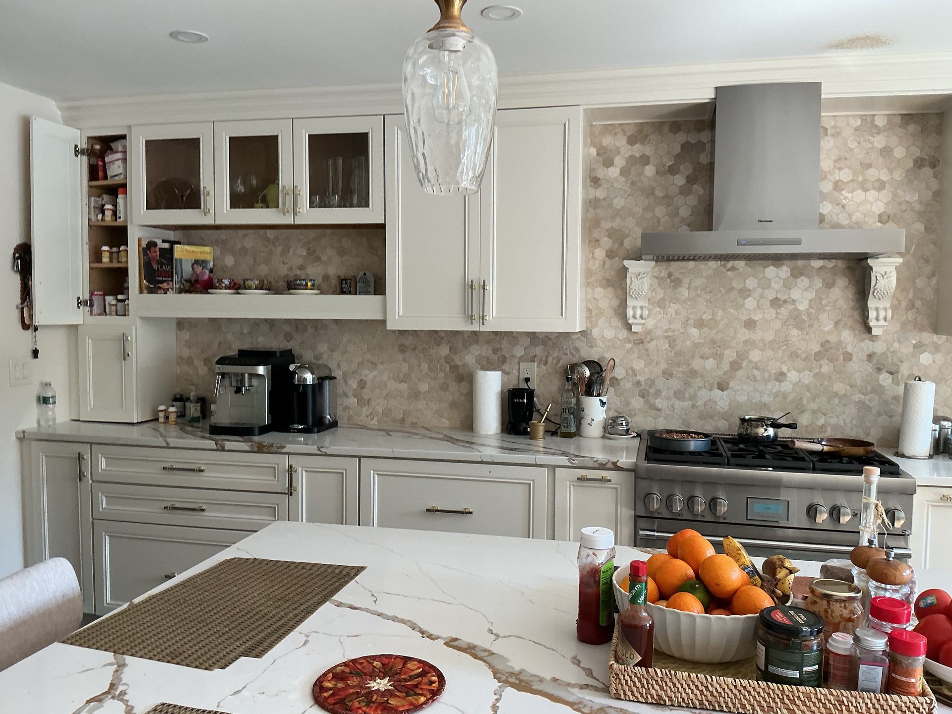 Bright kitchen with white cabinets, stove, island, and a basket of fruit and condiments on the counter