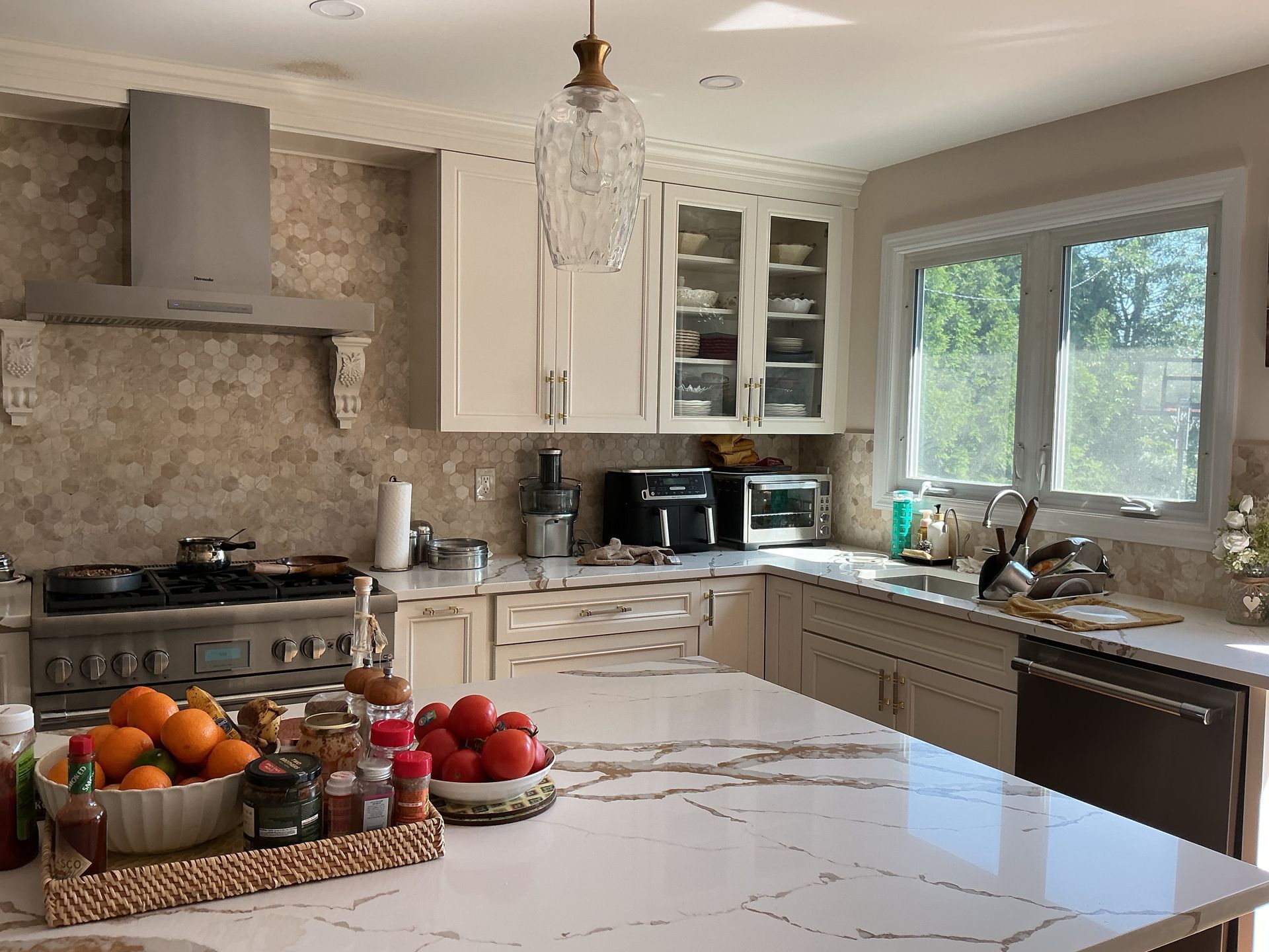 Bright modern kitchen with white island, stone backsplash, large window, and fruit bowls on the counter