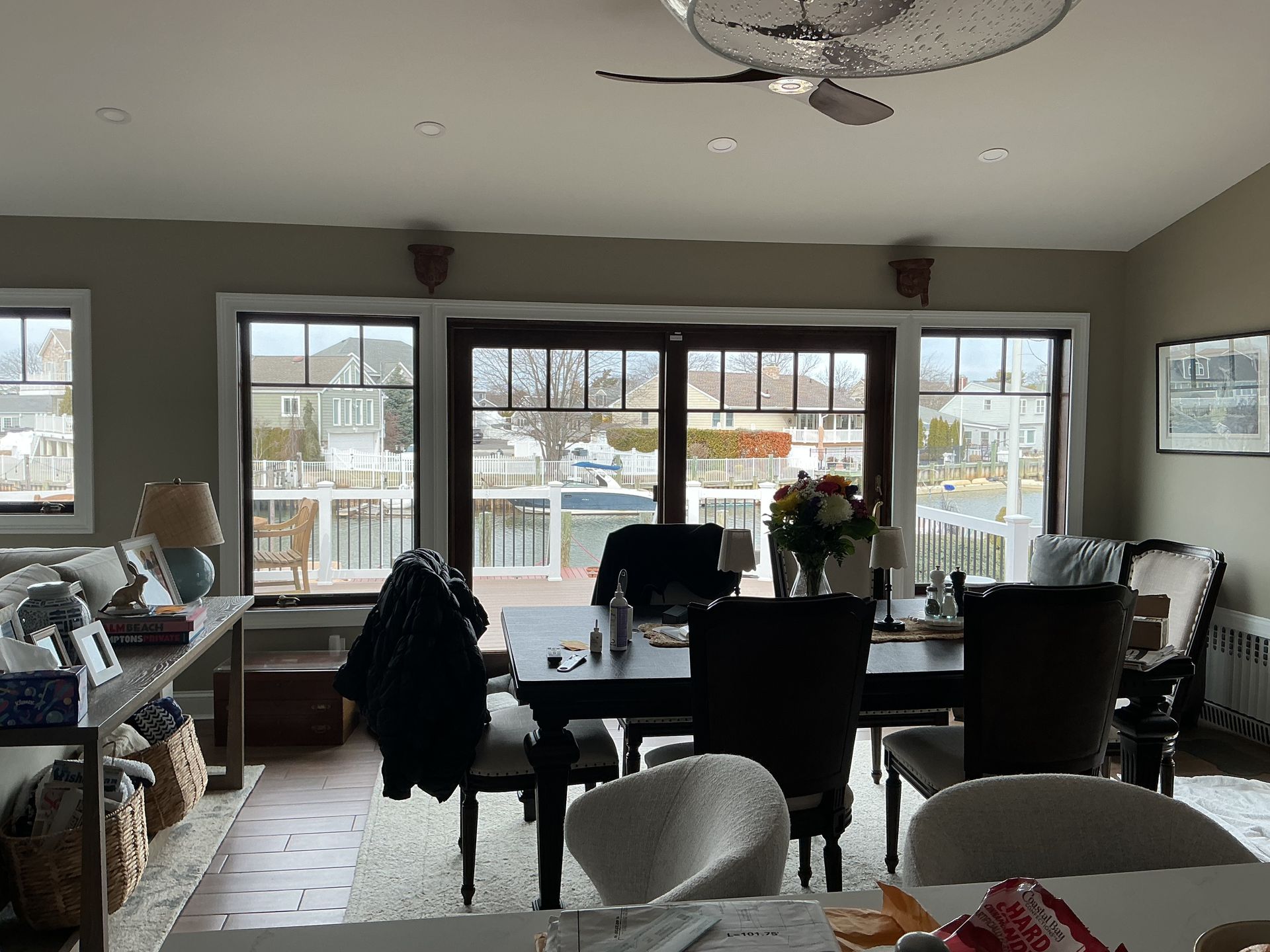 Dining area with table and chairs facing large windows, overlooking a deck and water.