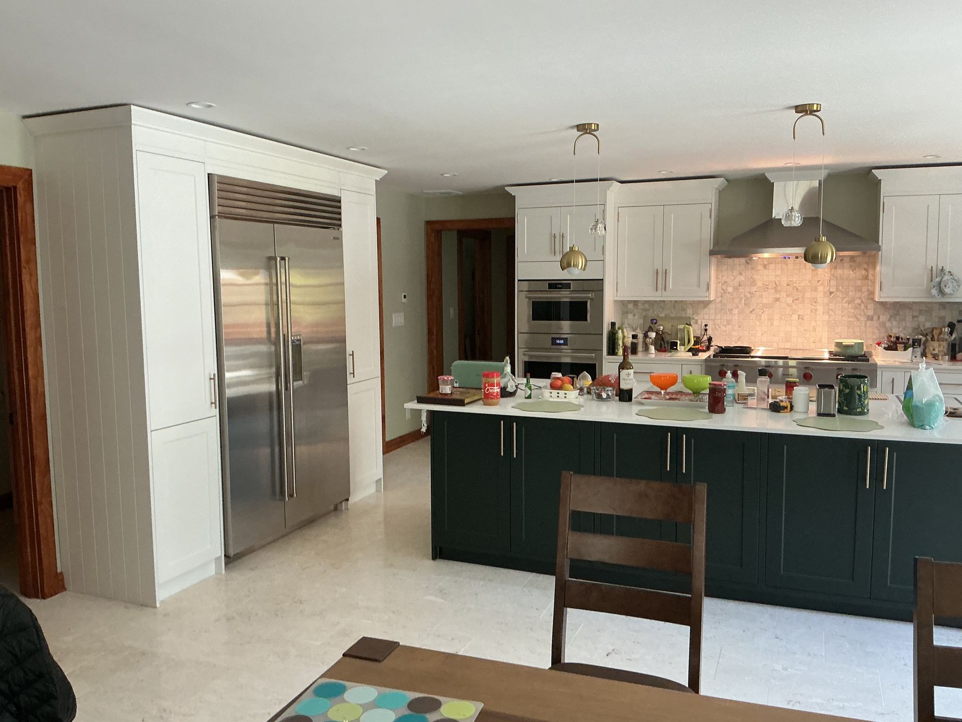 Modern kitchen with stainless fridge, dark island cabinets, and white countertops; chair in foreground