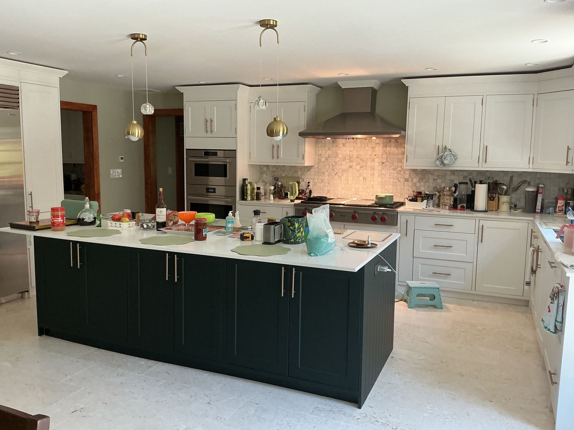 Bright kitchen with large island, white cabinets, stainless hood, and scattered items on counters and floor