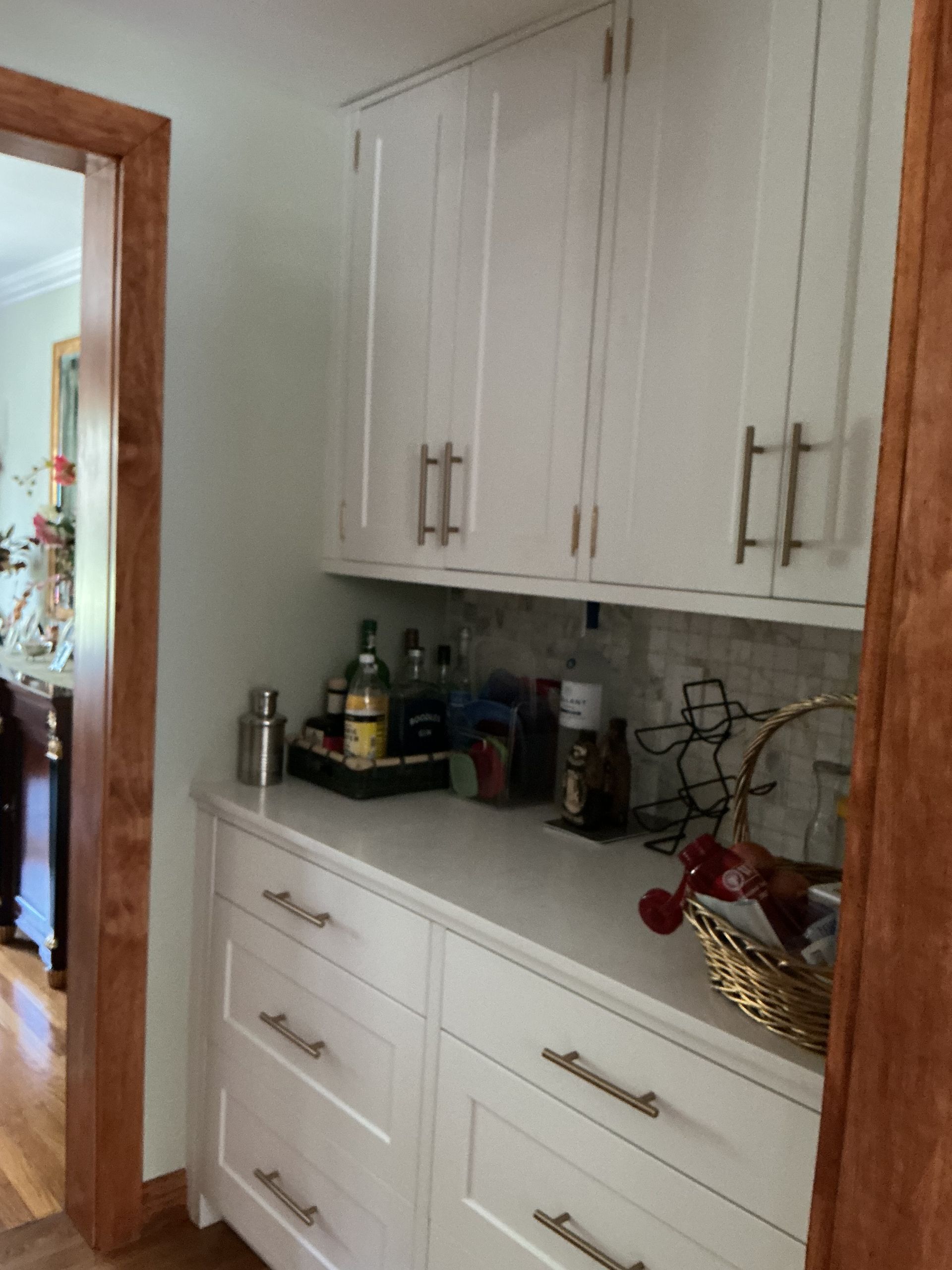 White kitchen cabinet with countertop items beside a doorway and hallway view