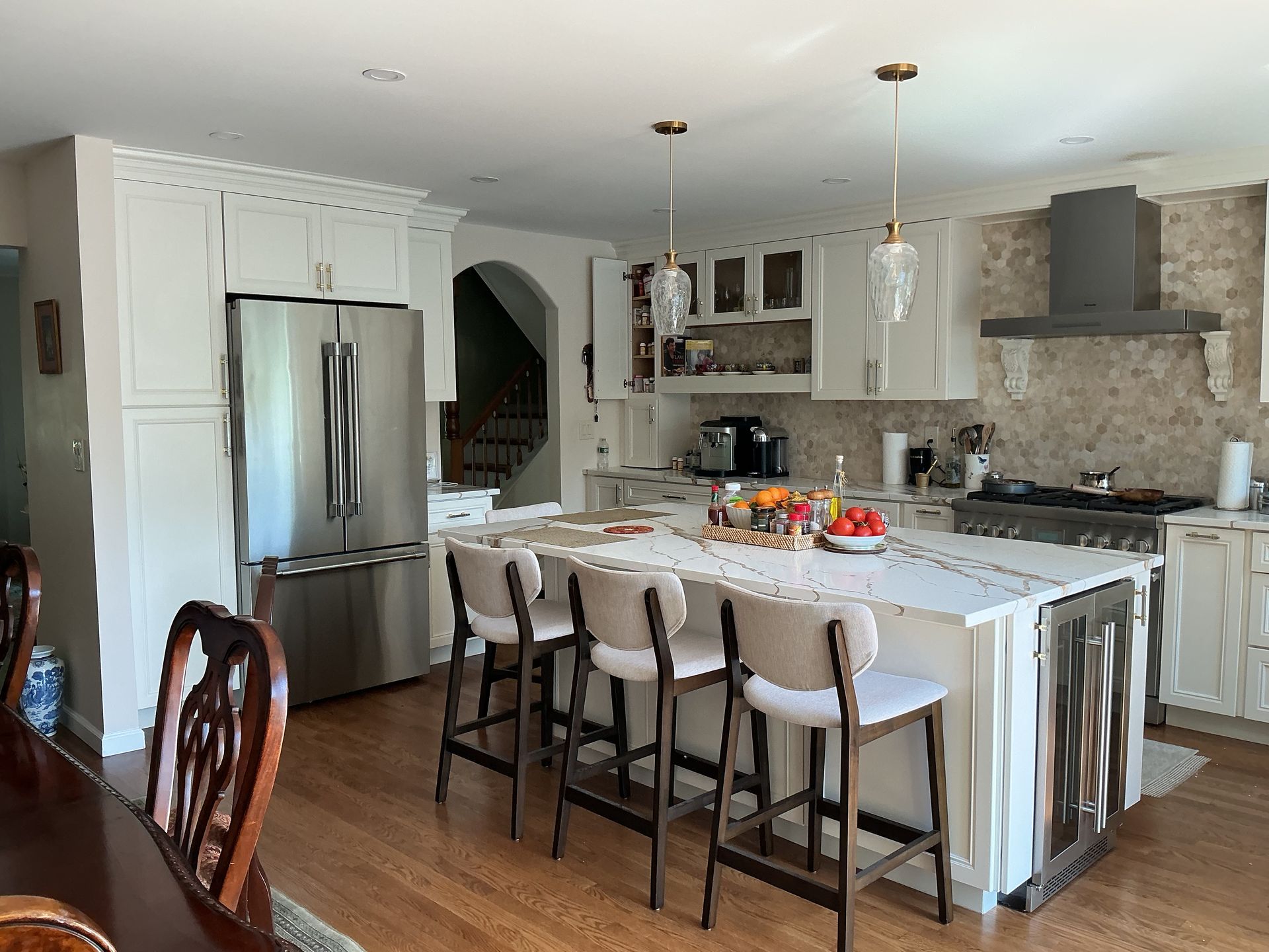 Modern kitchen with stainless steel fridge, white island, bar stools, and stone backsplash