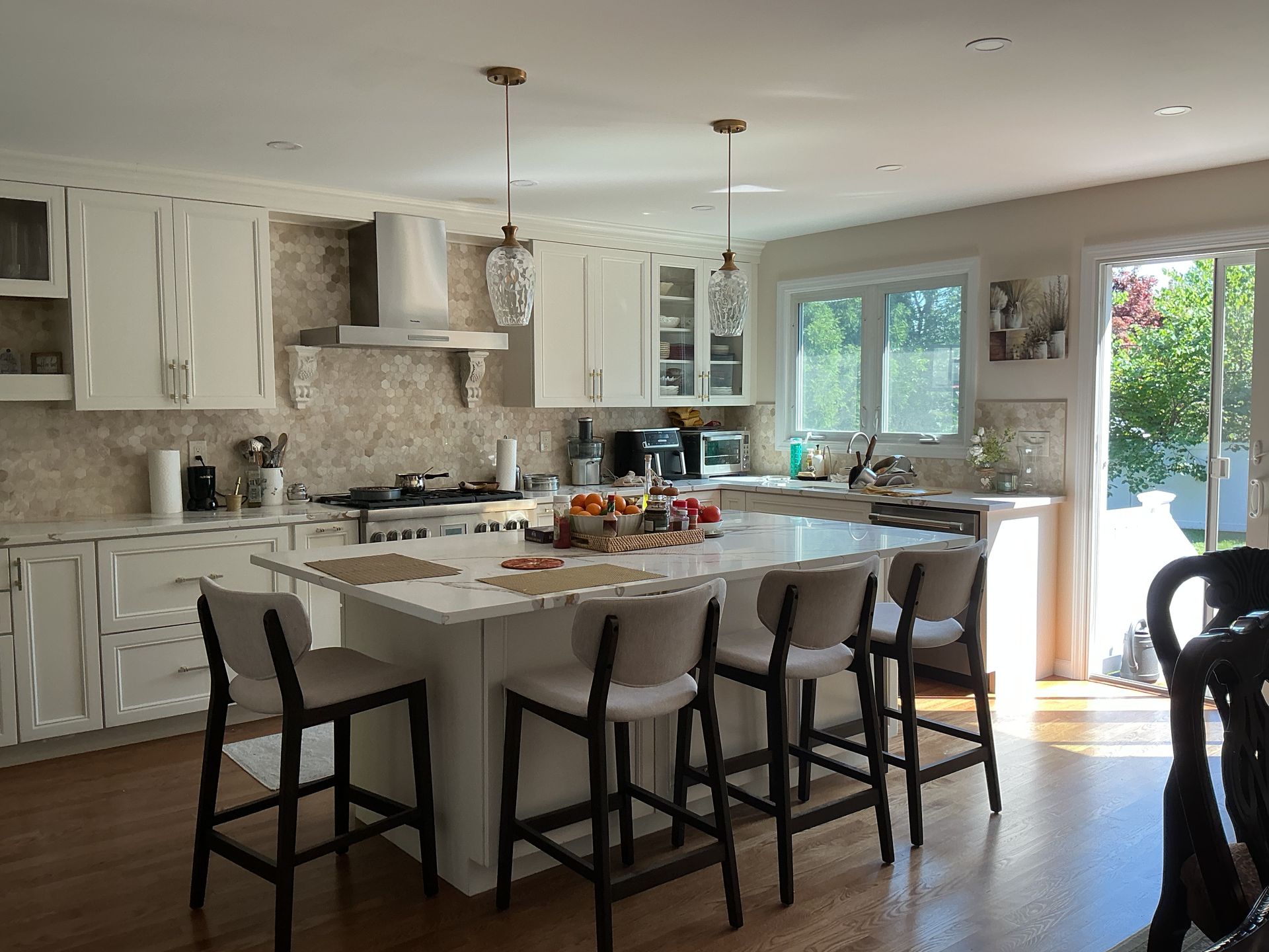 Bright modern kitchen with white cabinets, stone island, and bar stools by large windows and sliding doors