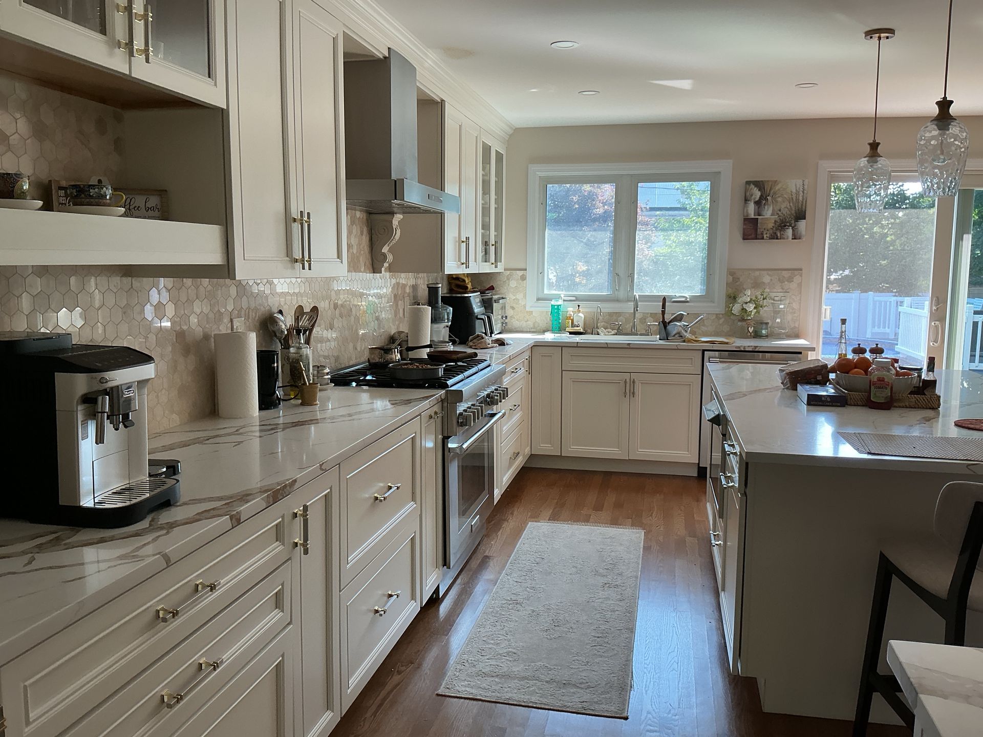 Bright kitchen with white cabinets, marble counters, island, and a window over the sink