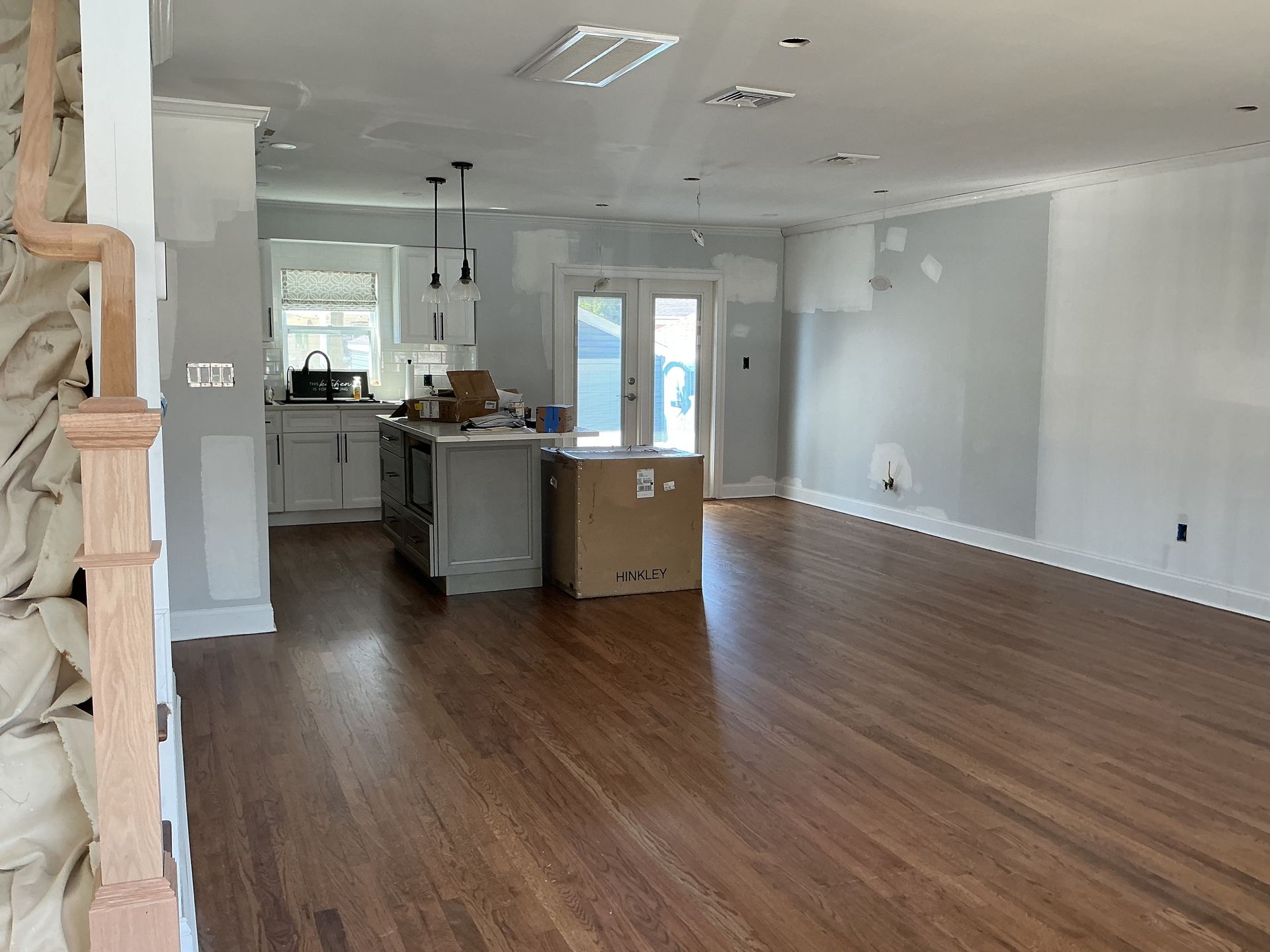 Empty open-plan living room with hardwood floors, white walls, and a kitchen island in the background