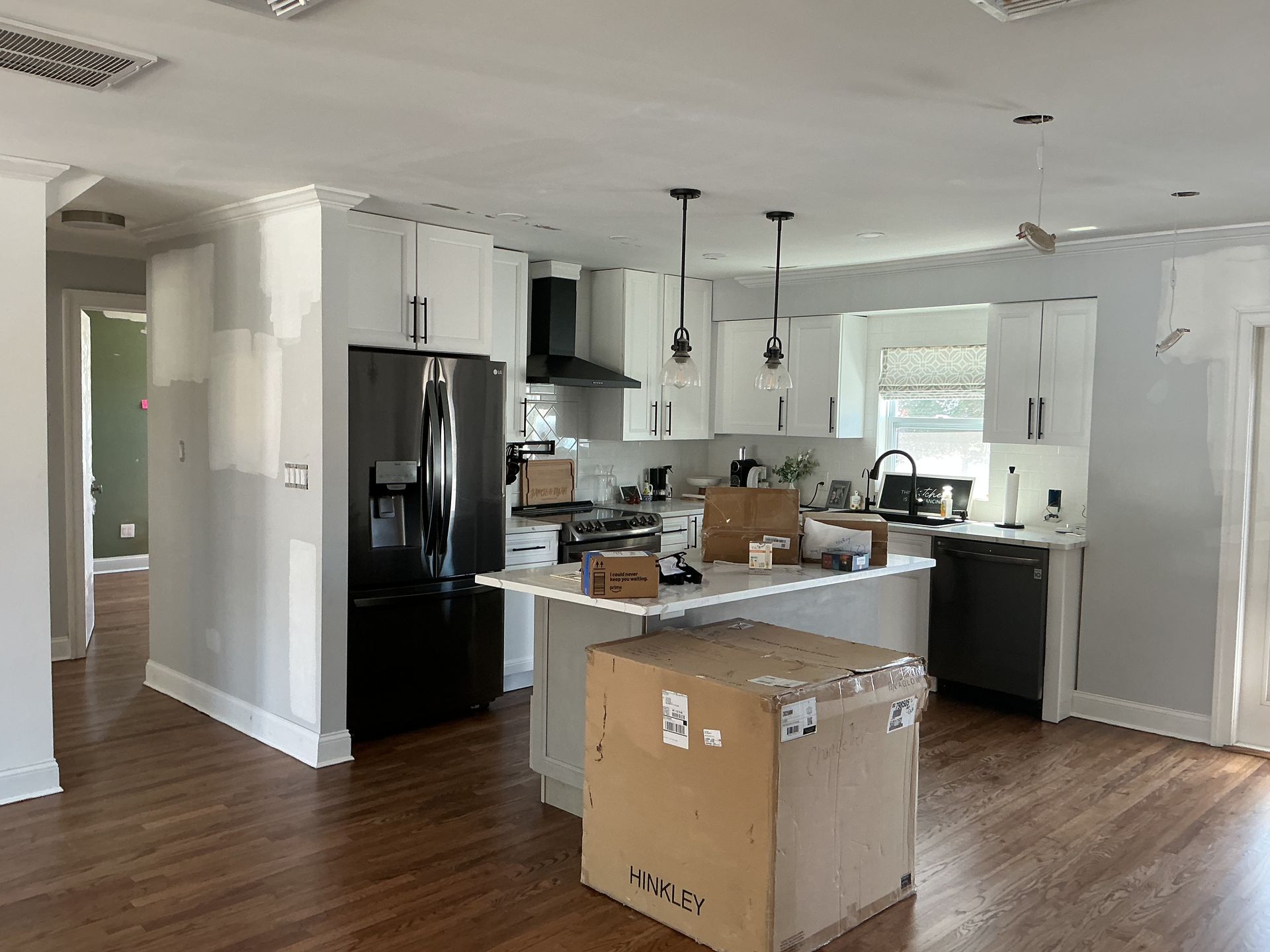 Unfinished kitchen with white cabinets, black appliances, wood floors, and moving boxes on the counter and floor