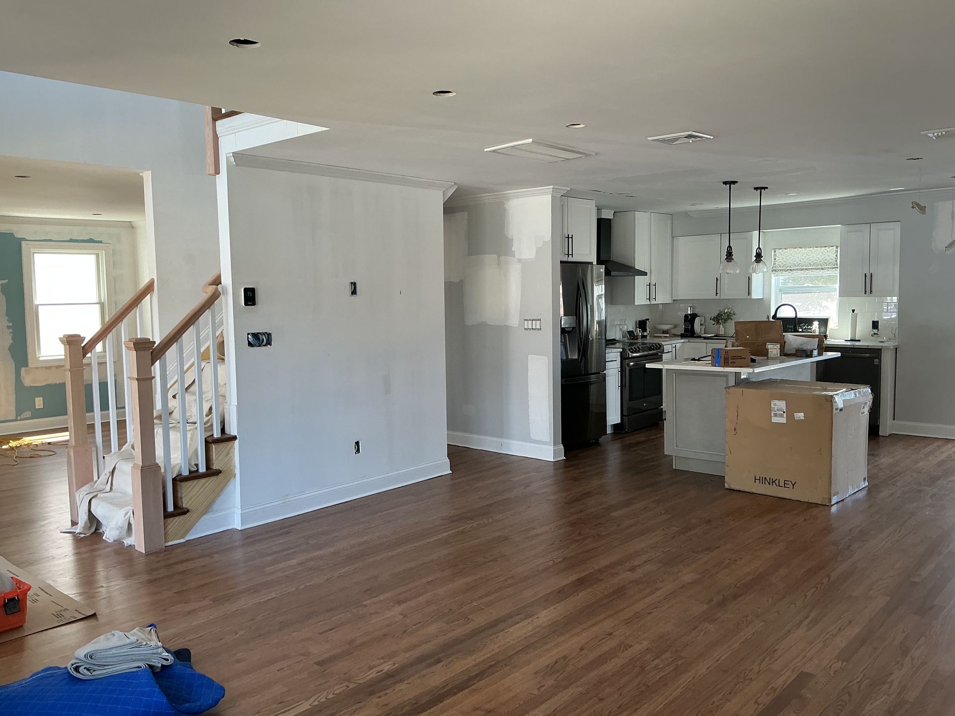 Empty open-plan living room and kitchen with wood floors, white walls, and a staircase on the left.