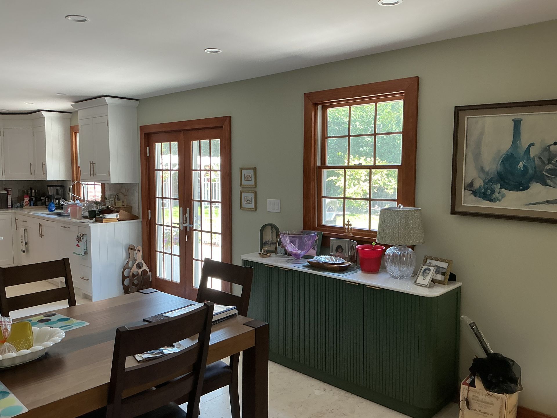 Dining room with wooden table, green sideboard, windows, and a view into a kitchen area