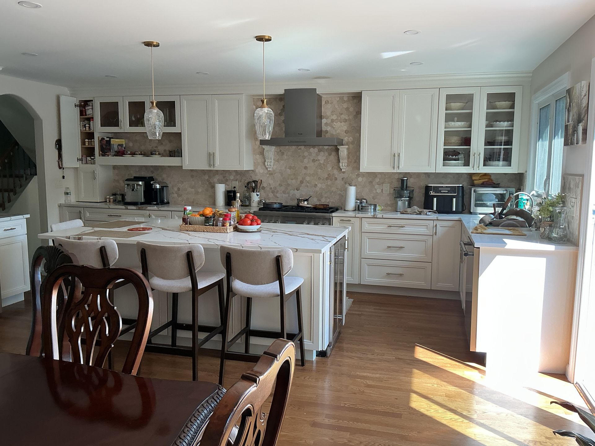 Bright kitchen with white cabinets, island stools, and sunlight on the wooden floor