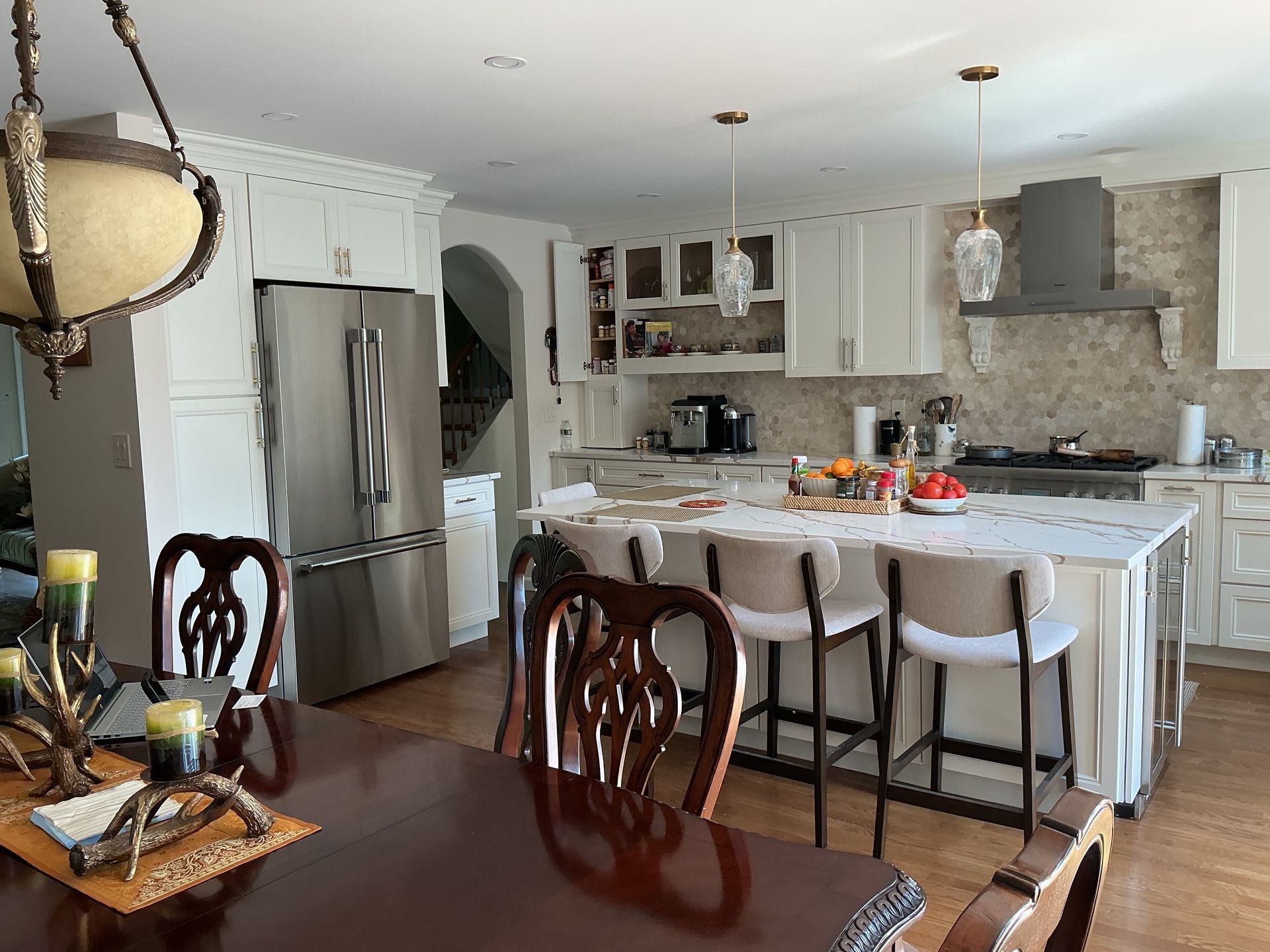 Bright kitchen with white cabinets, stainless fridge, marble island, bar stools, and adjacent dining table