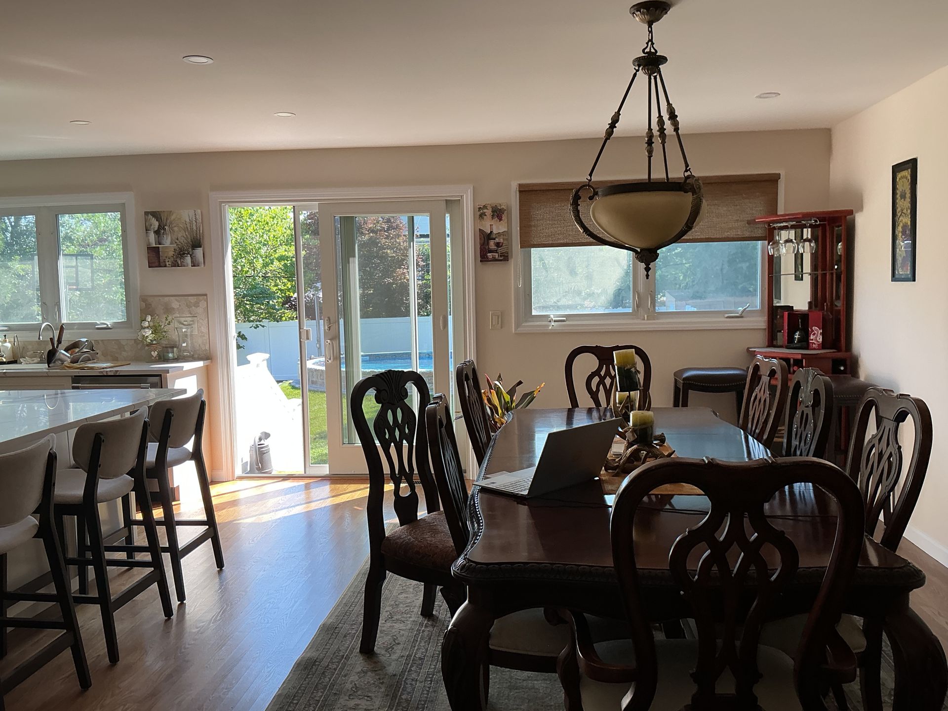 Bright dining room with dark wood table, chairs, a chandelier, and open doors to a sunlit patio.