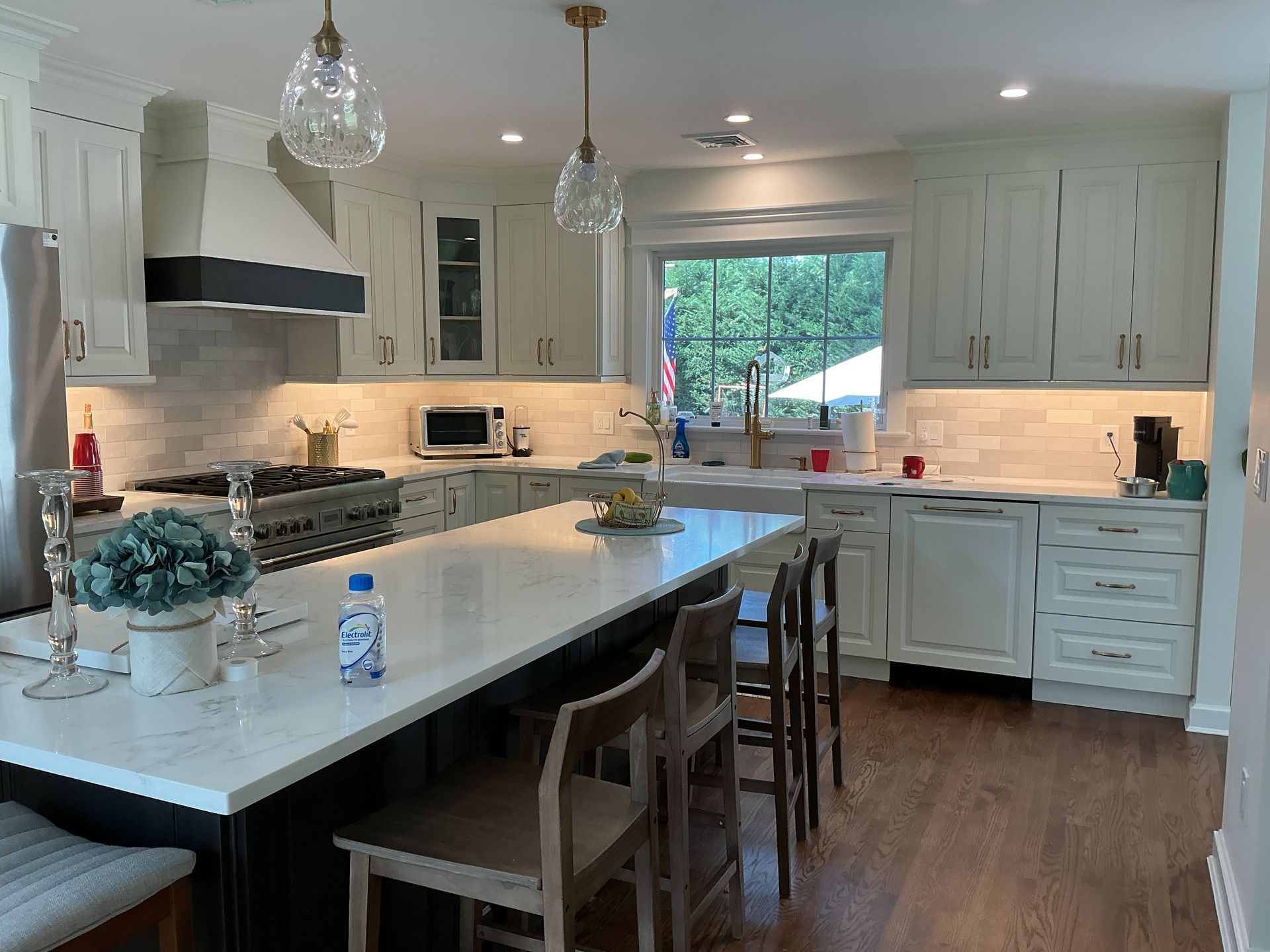 Bright white kitchen with island, pendant lights, barstools, and sunlit window over the sink